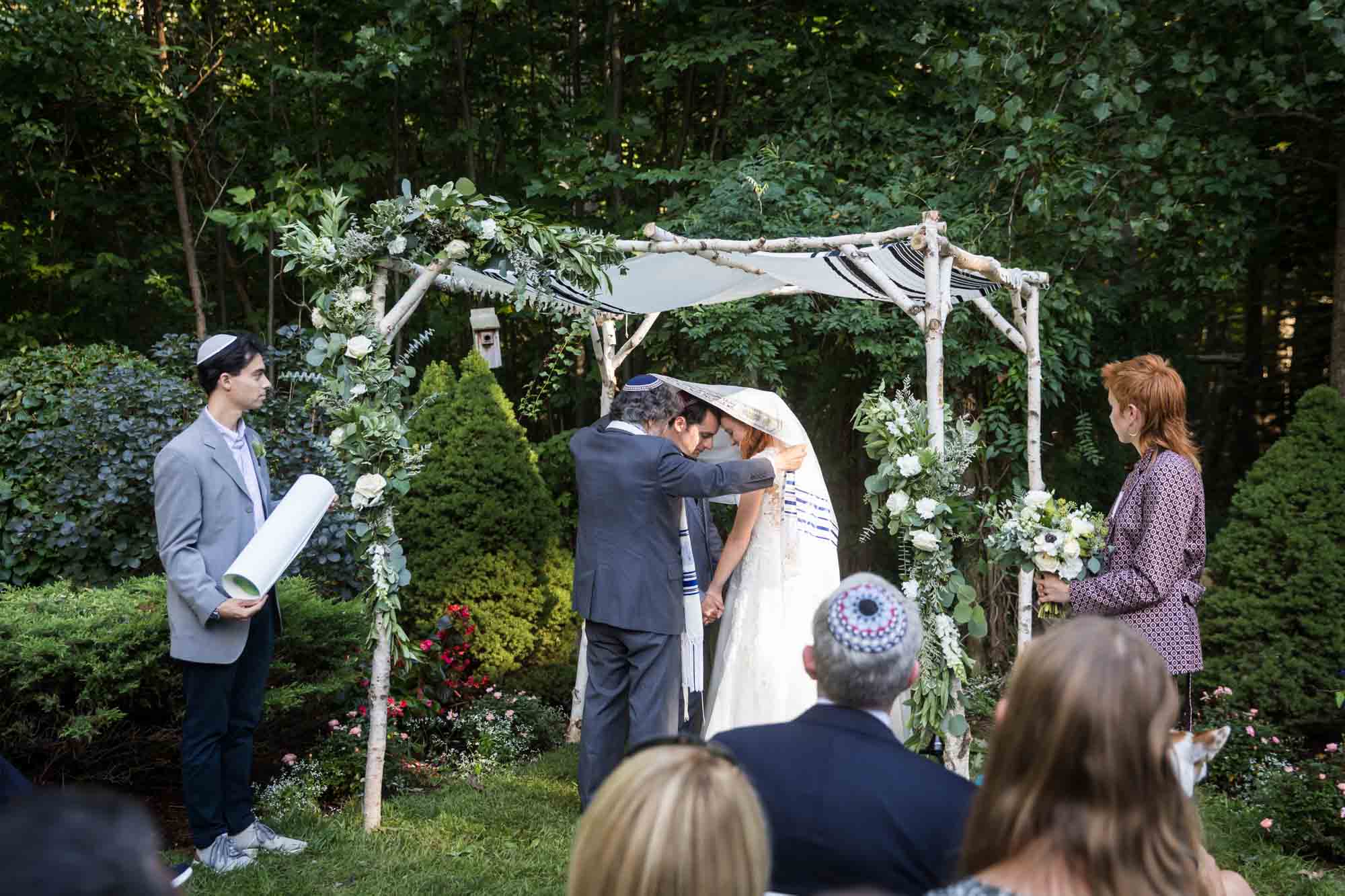 Bride and groom under prayer shawl and chuppah during ceremony