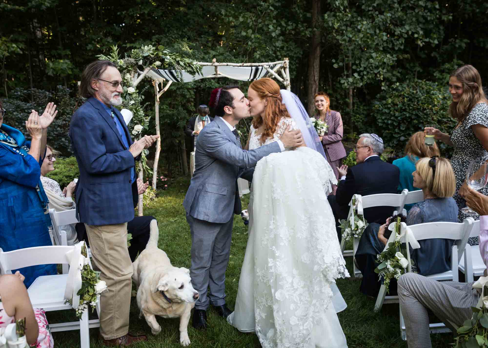 Bride and groom kissing in aisle in front of guests and dog during ceremony