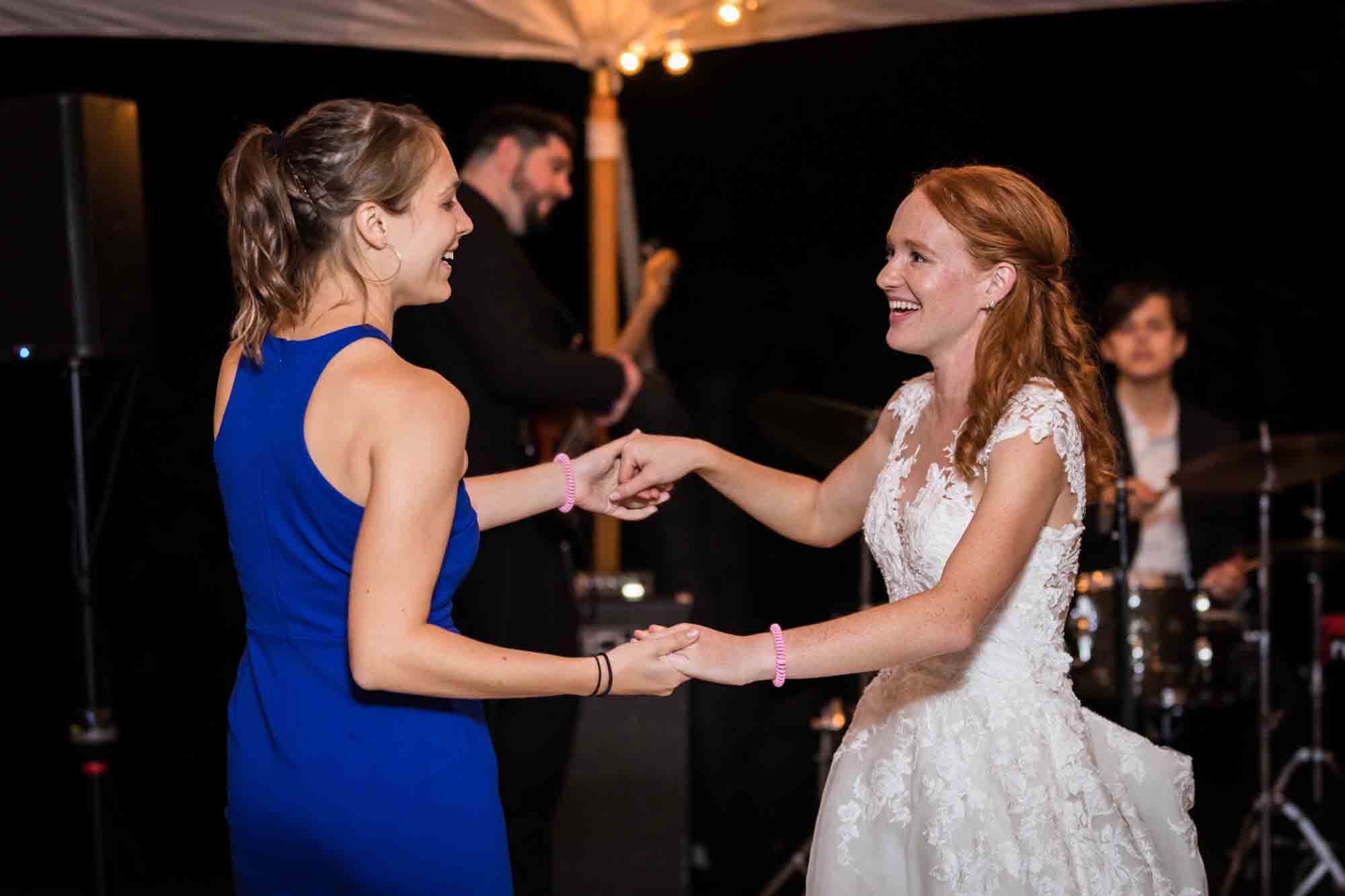 Bride and woman in blue dress holding hands and dancing
