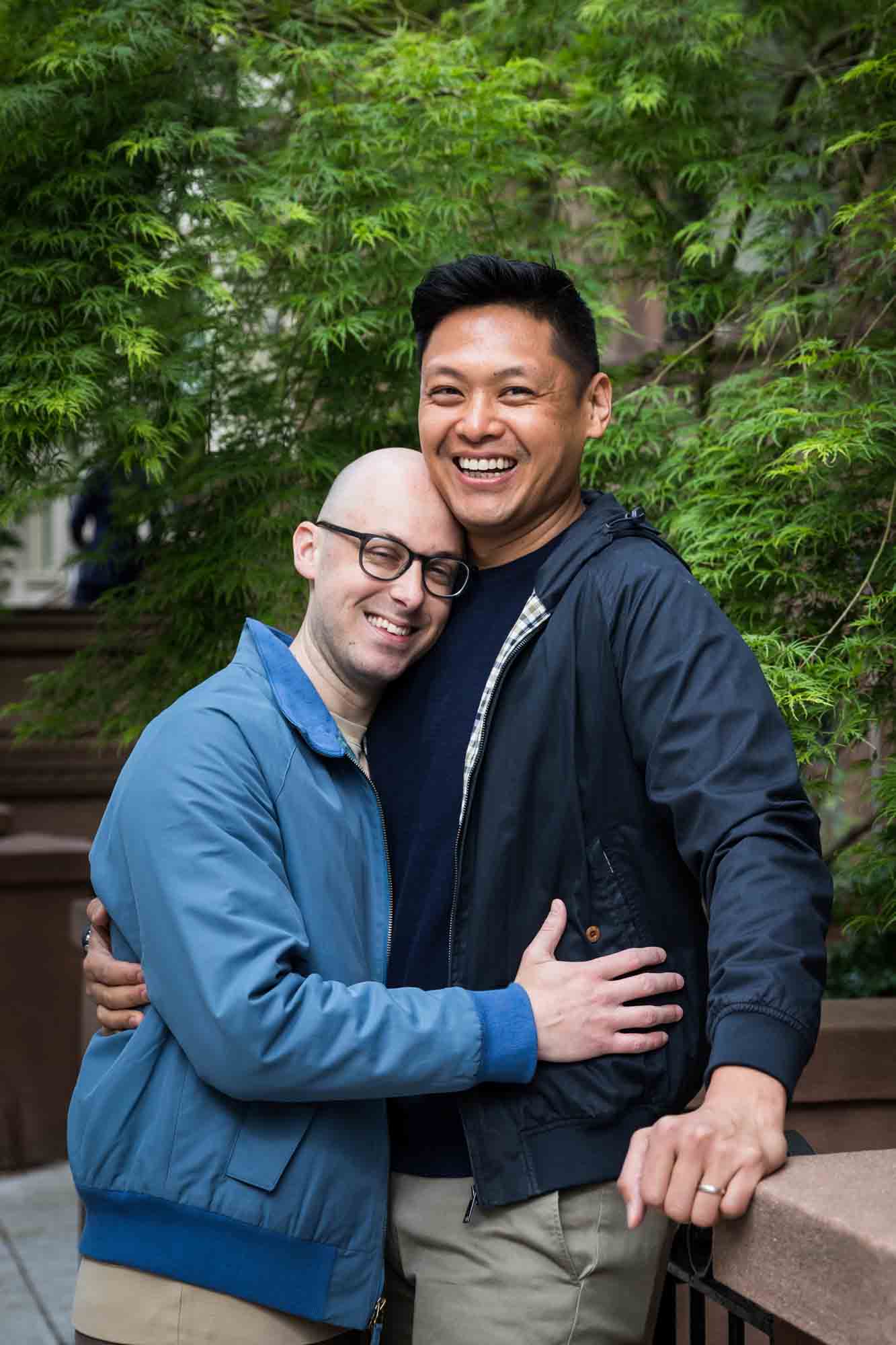 Two men hugging on sidewalk with tree in background