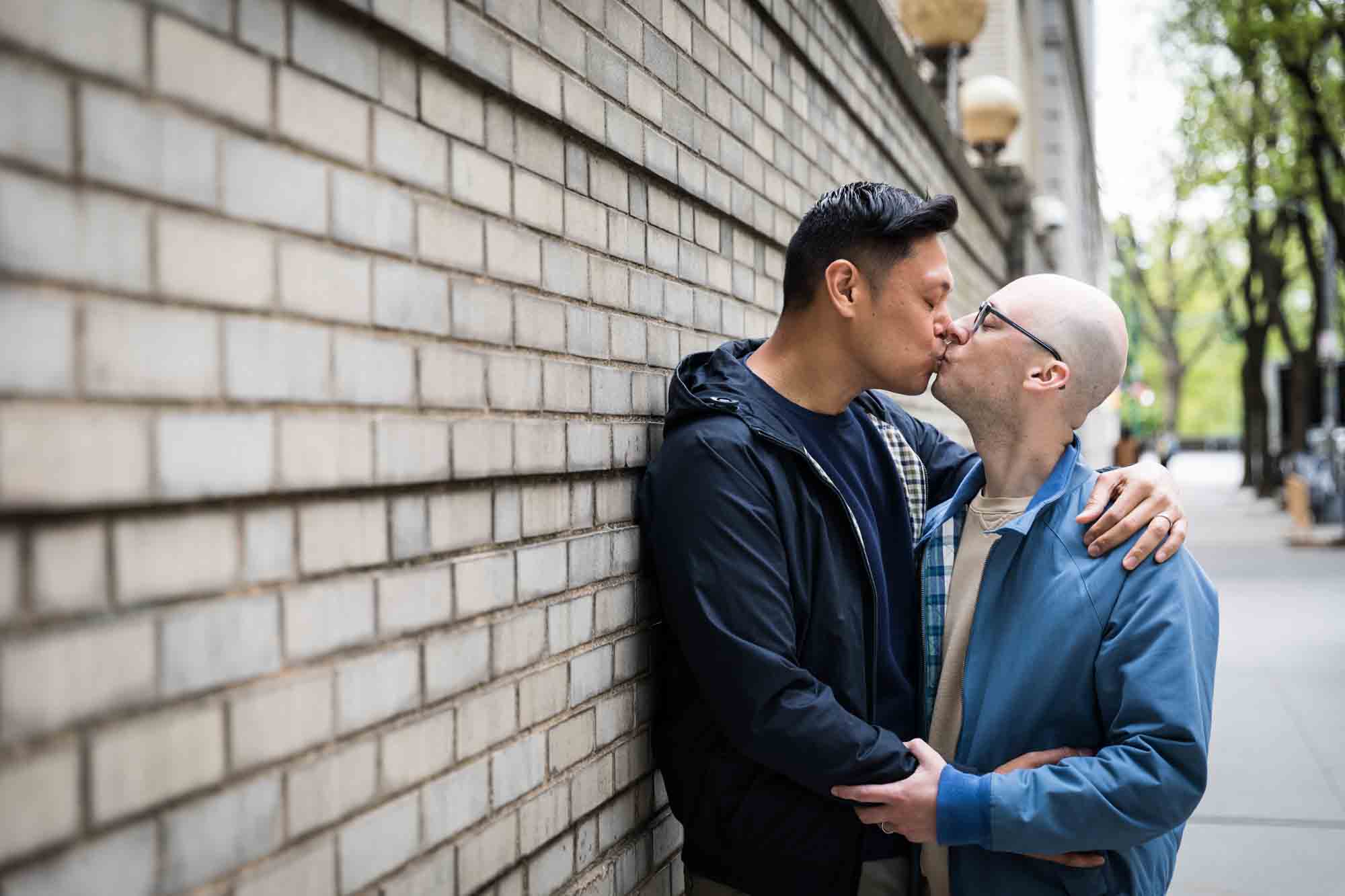 Two men kissing in front of brick wall