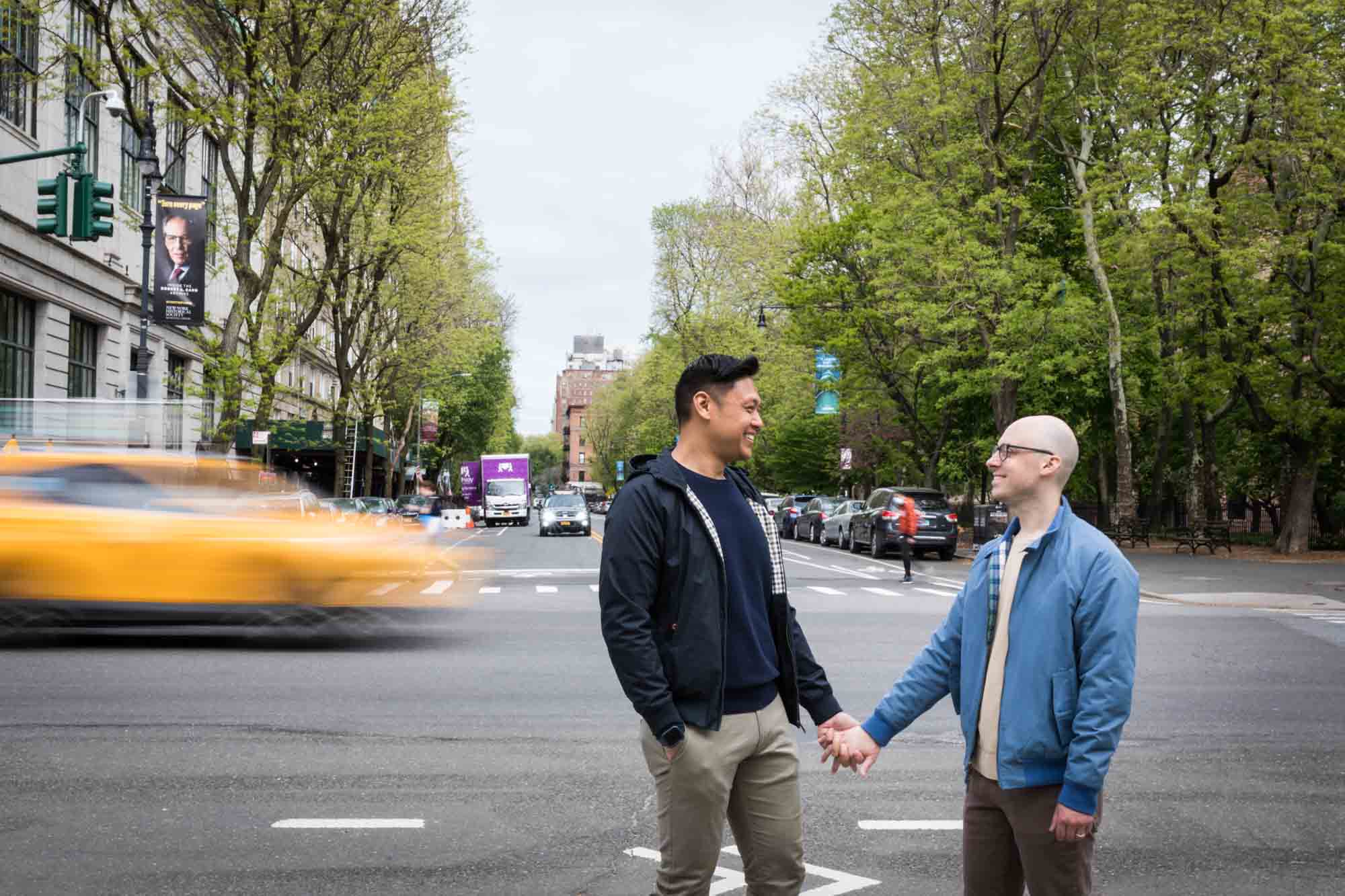 Two men holding hands with blurry taxicab in background