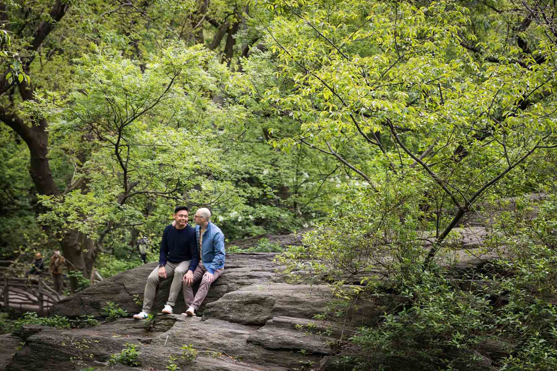 Two men sitting on rock ledge from a Central Park engagement photo shoot