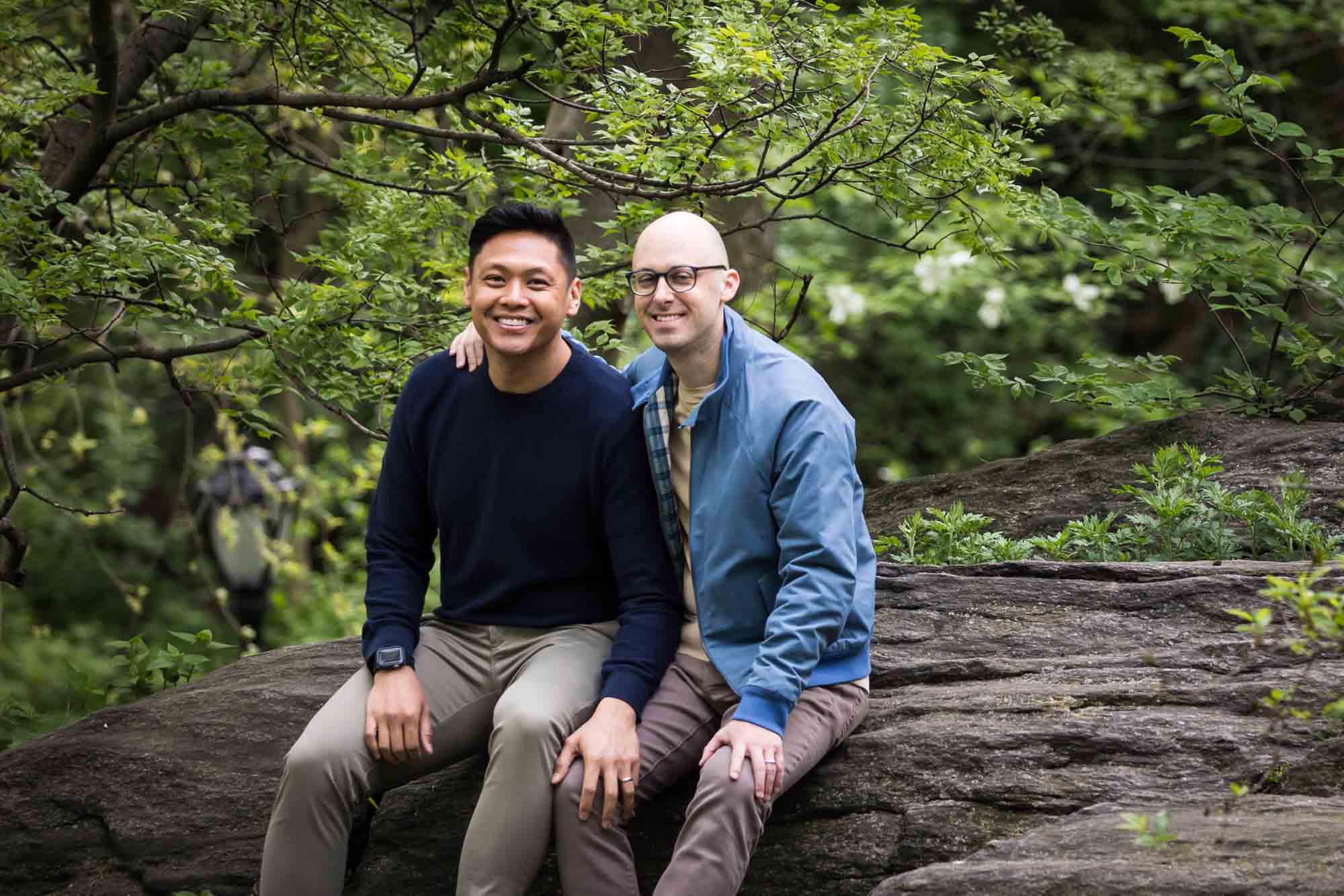 Two men sitting on rock ledge from a Central Park engagement photo shoot