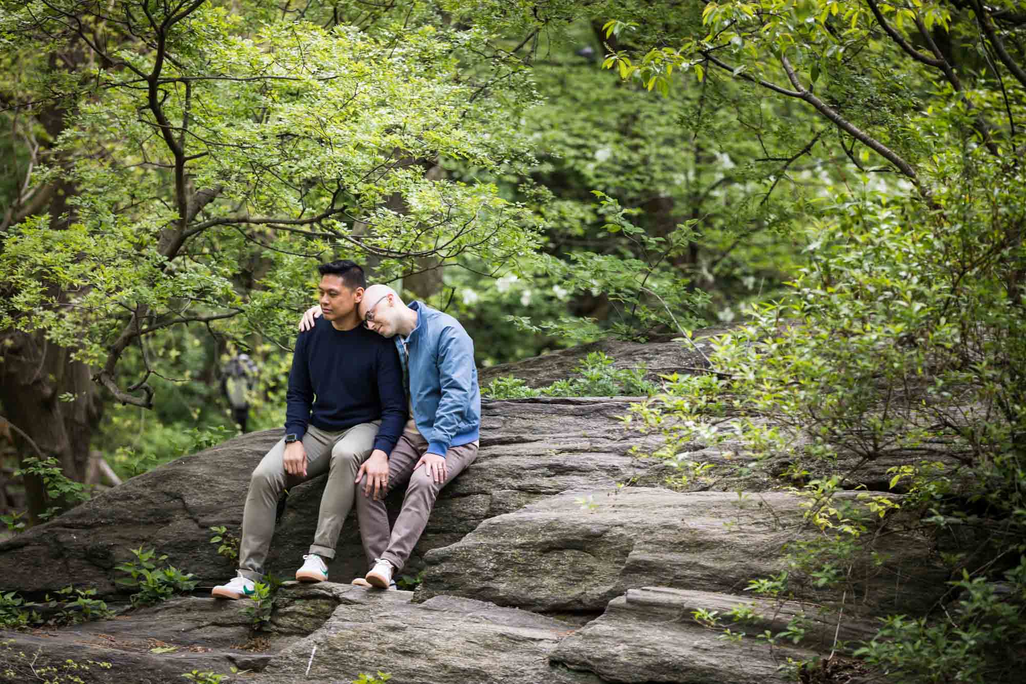 Two men sitting on rock ledge from a Central Park engagement photo shoot