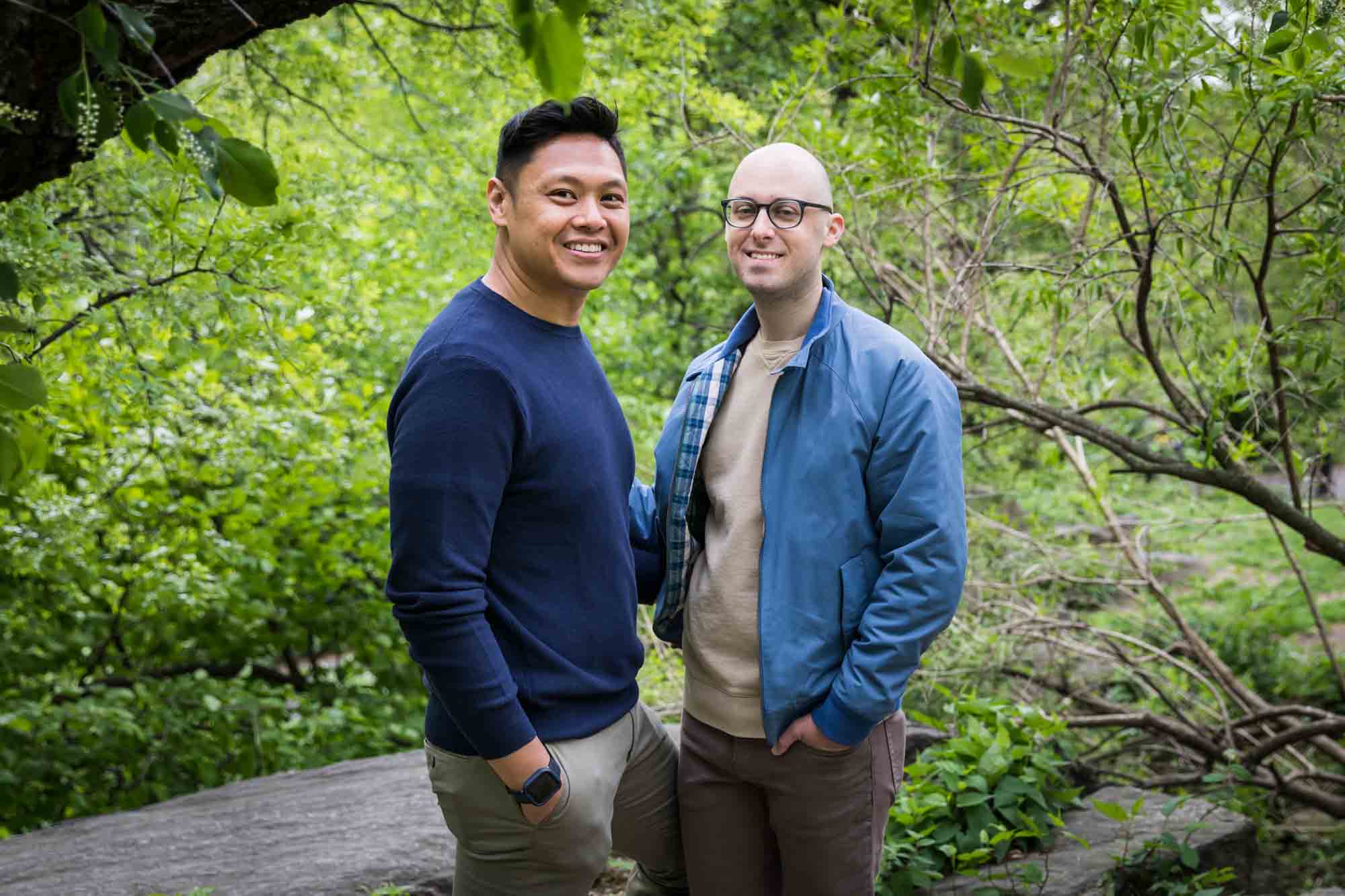 Two men holding hands surrounded by trees from a Central Park engagement photo shoot