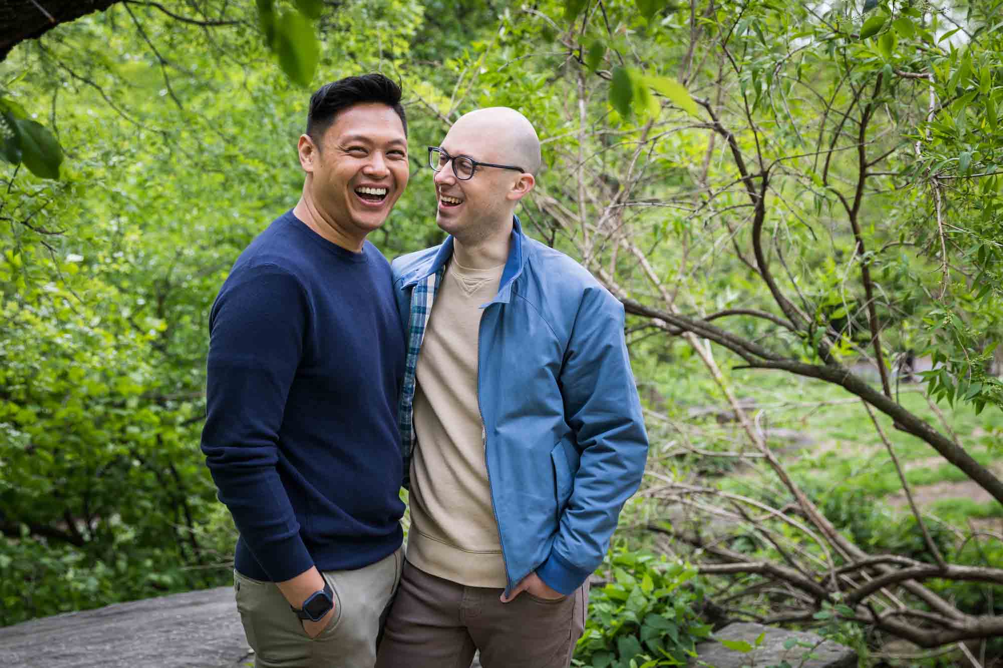 Two men dressed casually in forest from a Central Park engagement photo shoot