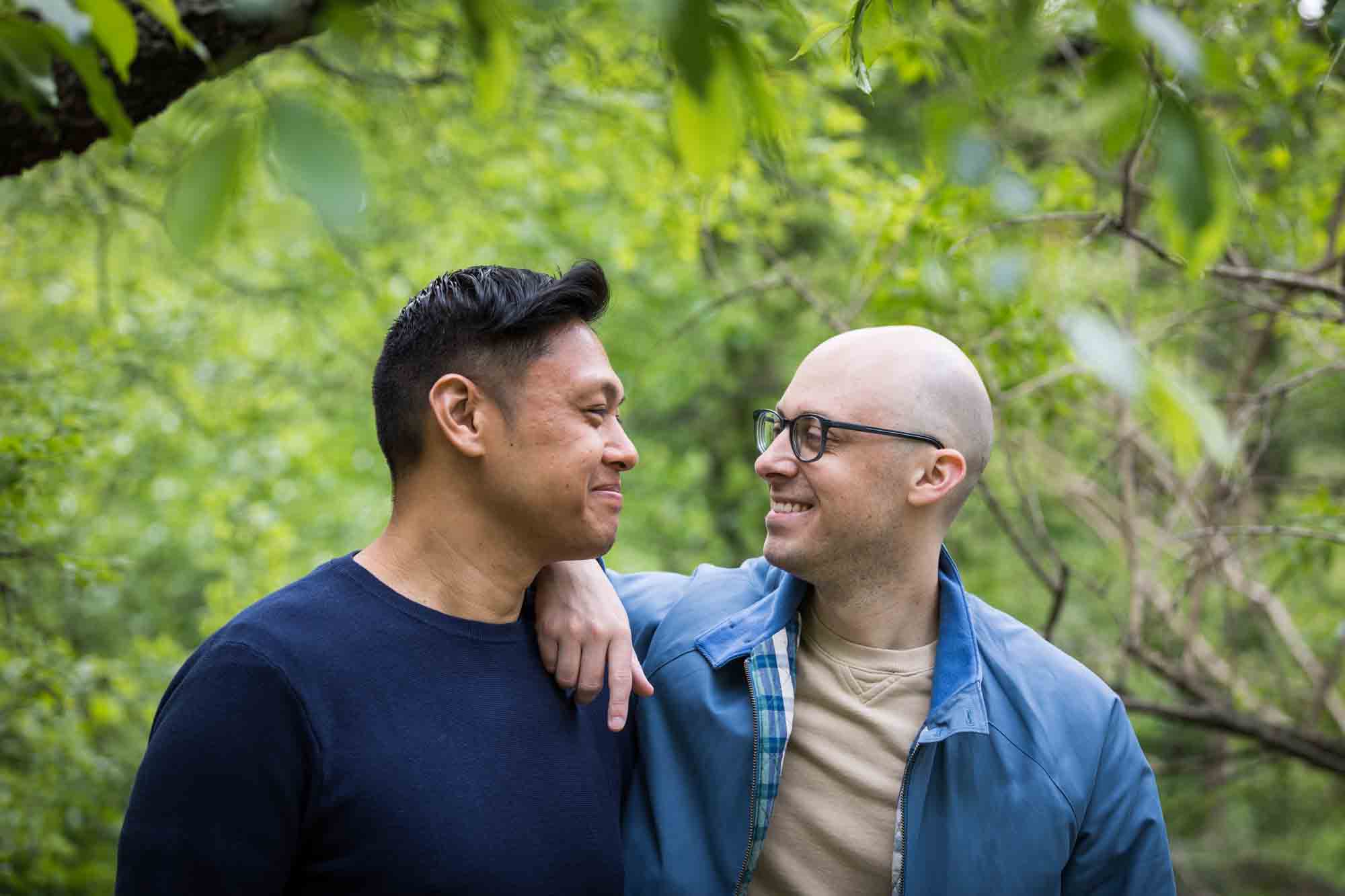 Two men wearing blue looking at each other from a Central Park engagement photo shoot