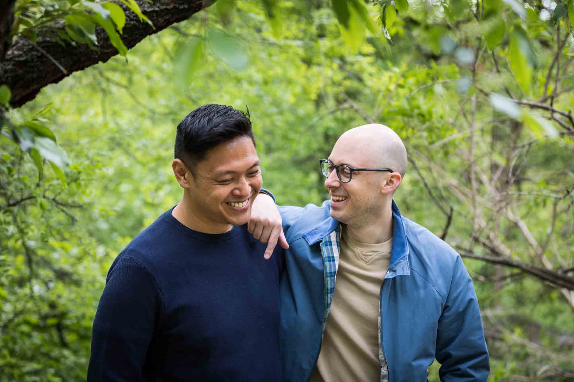Two men wearing blue and laughing from a Central Park engagement photo shoot