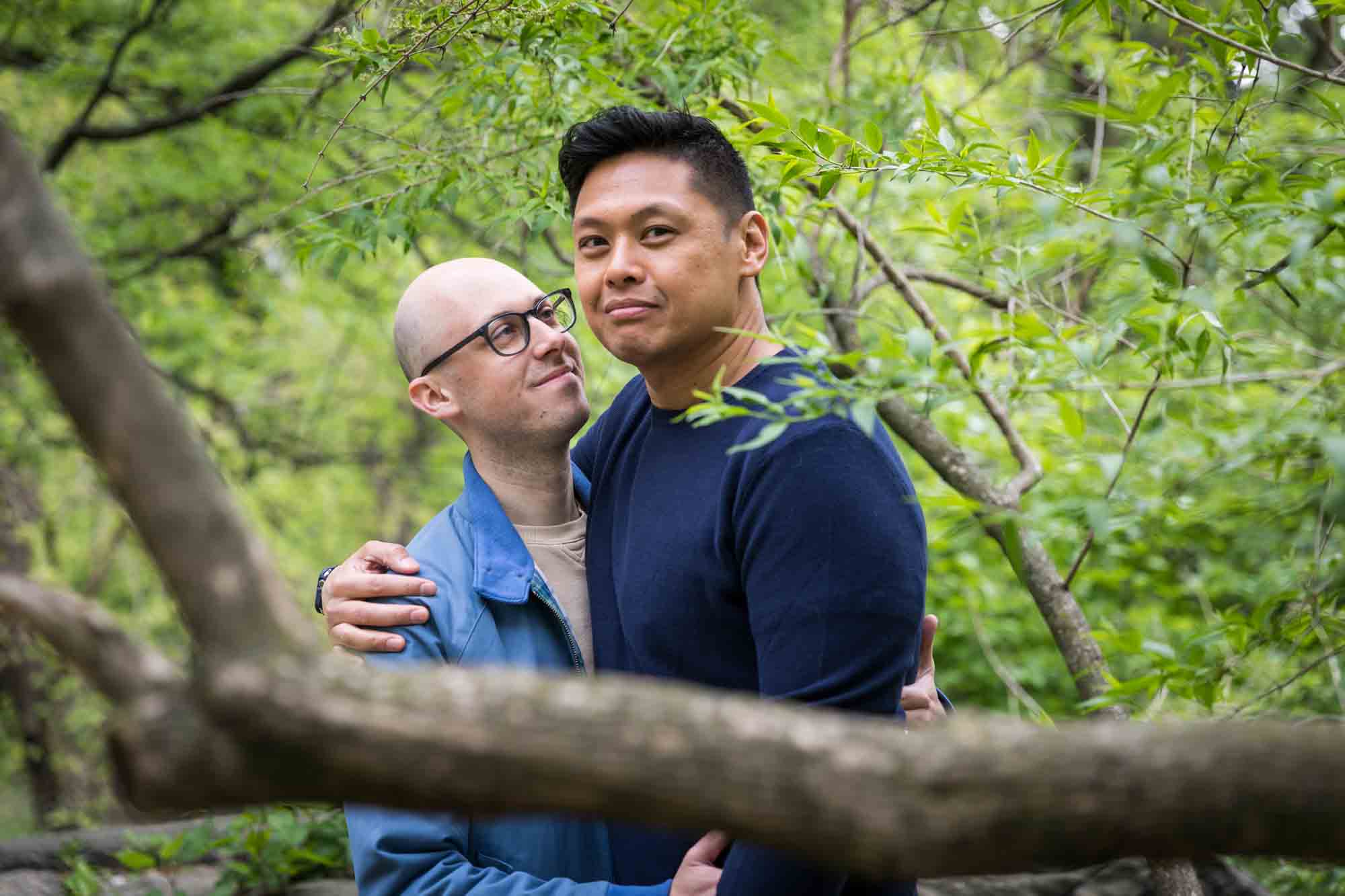Two men hugging behind a tree from a Central Park engagement photo shoot