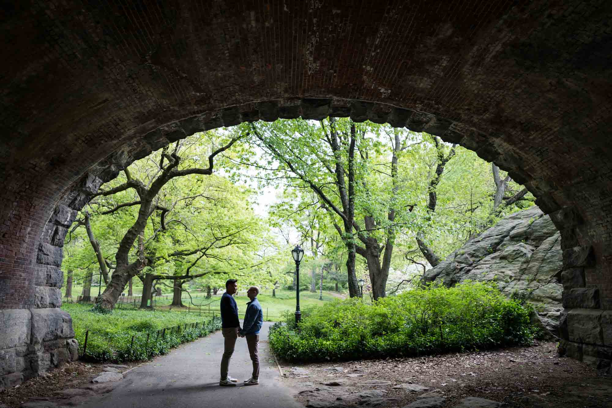 Two men standing under archway from a Central Park engagement photo shoot