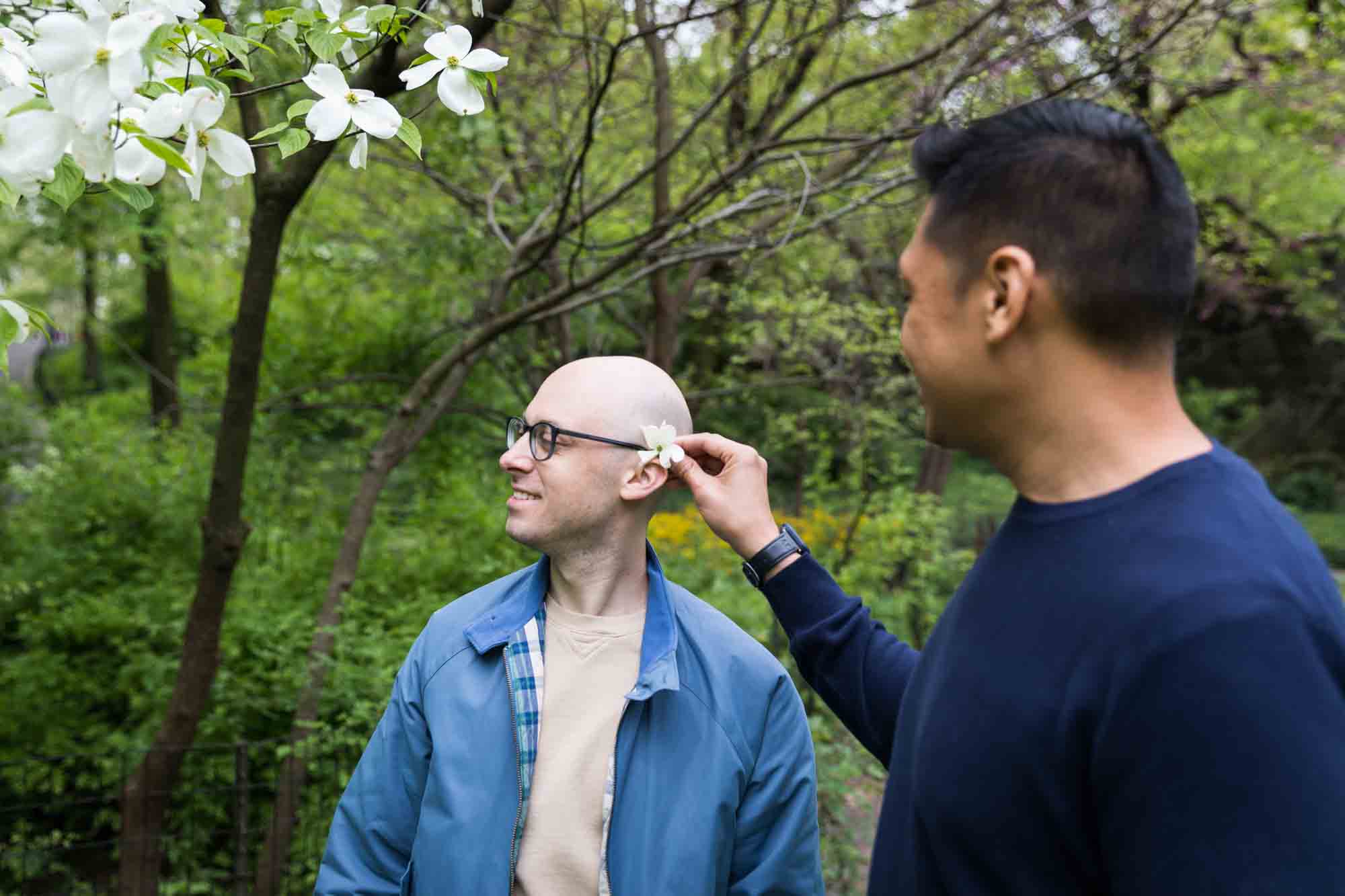 Man putting flower behind other man's ear