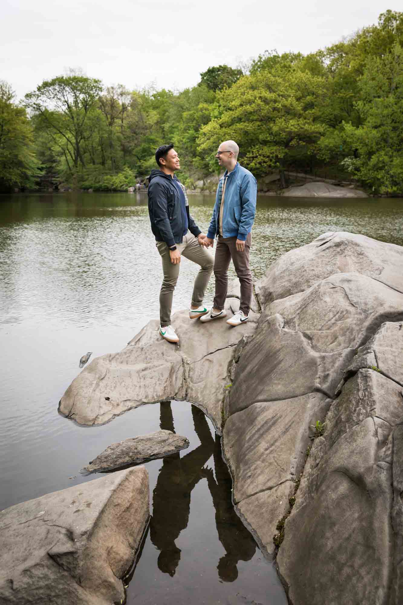 Two men standing on rock with reflection in water