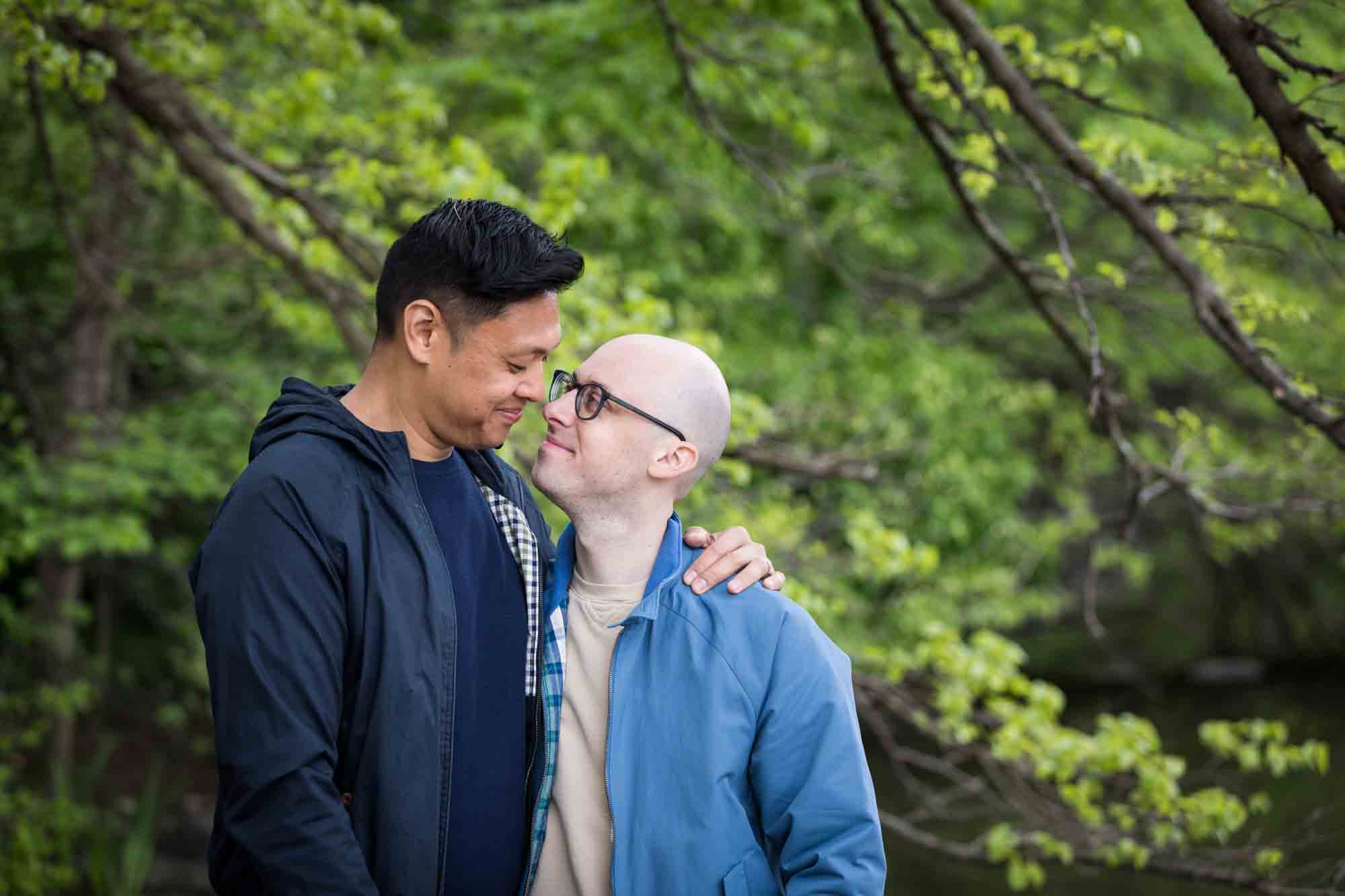 Two men hugging in front of tree branches from a Central Park engagement photo shoot