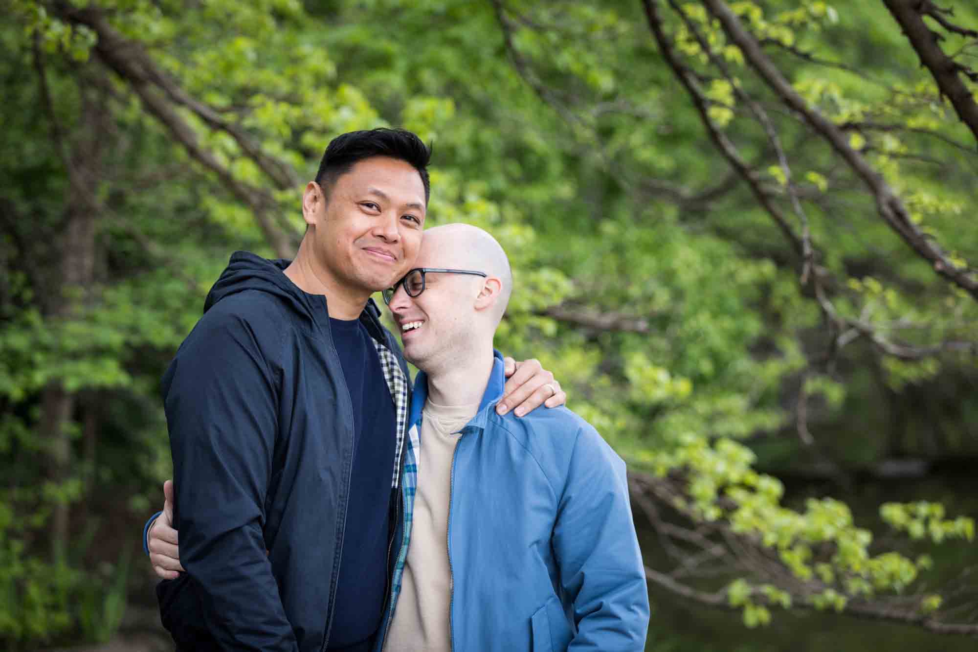 Two men embracing in front of tree branches from a Central Park engagement photo shoot