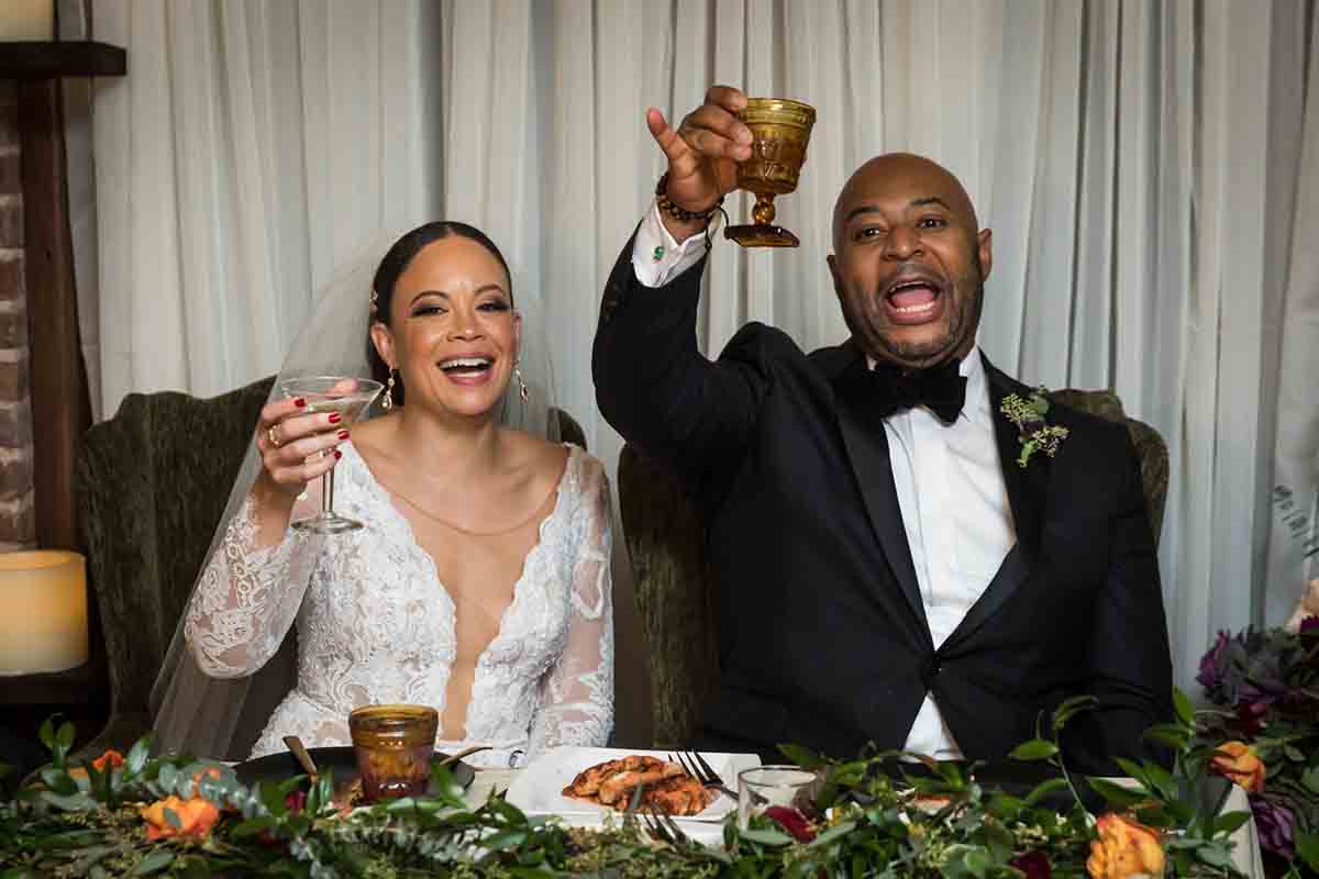 Bride and groom raising glasses to guests at a Deity wedding