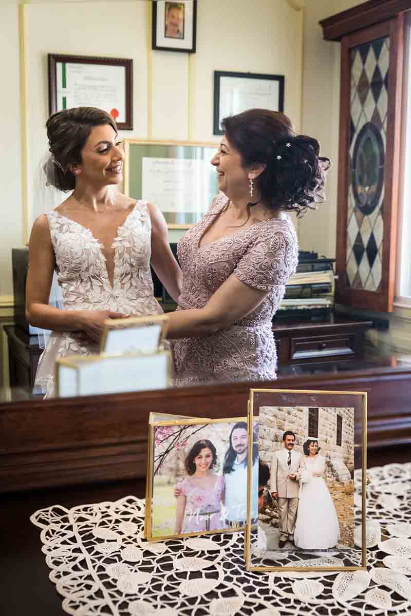 Bride and mother reflected in mirror in front of family photos on dresser