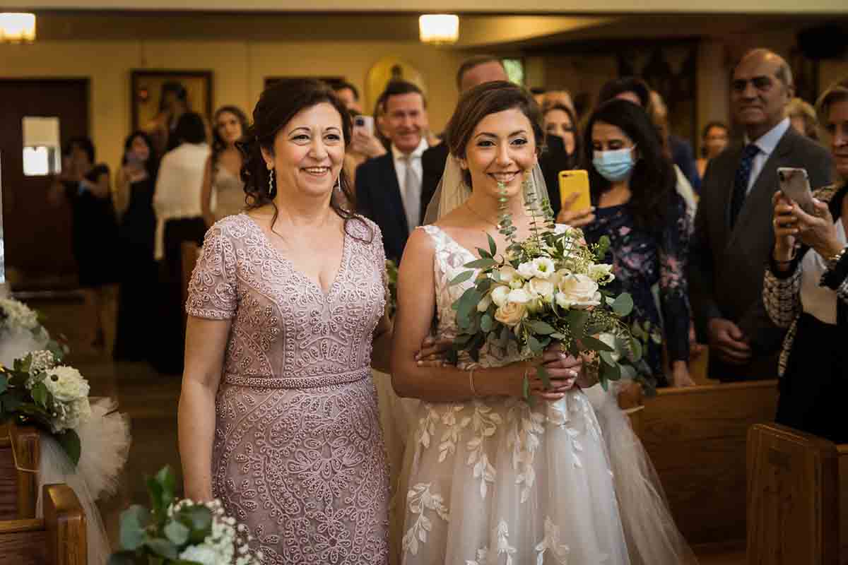 Bride and mother coming down aisle during eastern orthodox wedding ceremony