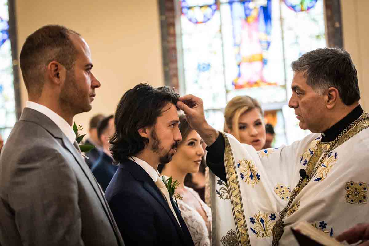 Priest making sign of cross on groom's forehead during eastern orthodox wedding ceremony