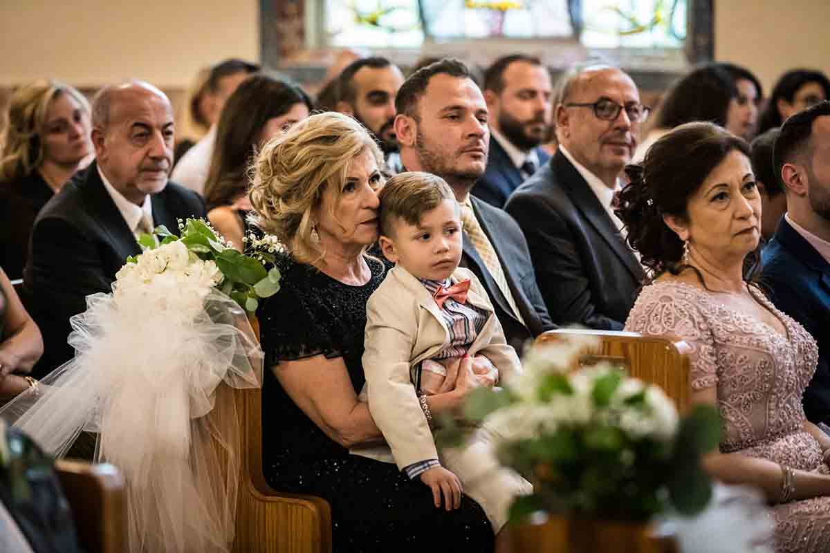 Older woman holding boy on lap during eastern orthodox wedding ceremony
