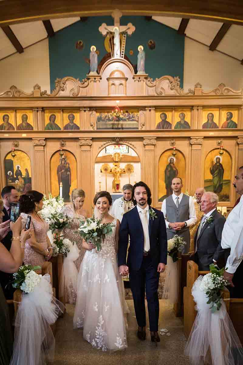 Bride and groom recessing down aisle during eastern orthodox wedding ceremony