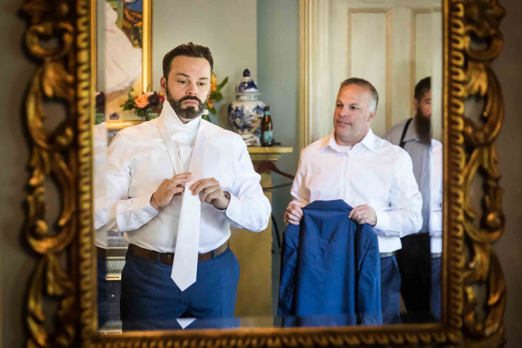 Groom and groomsmen putting on tie at a FEAST at Round Hill wedding