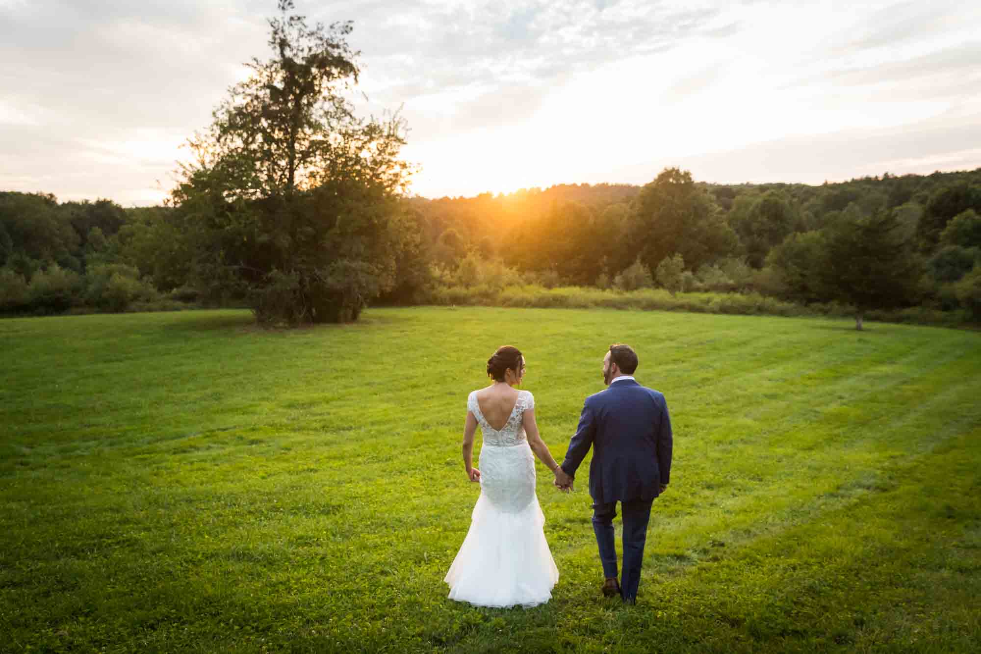 Bride and groom walking across meadow at sunset for an article on how to relax in front of the camera