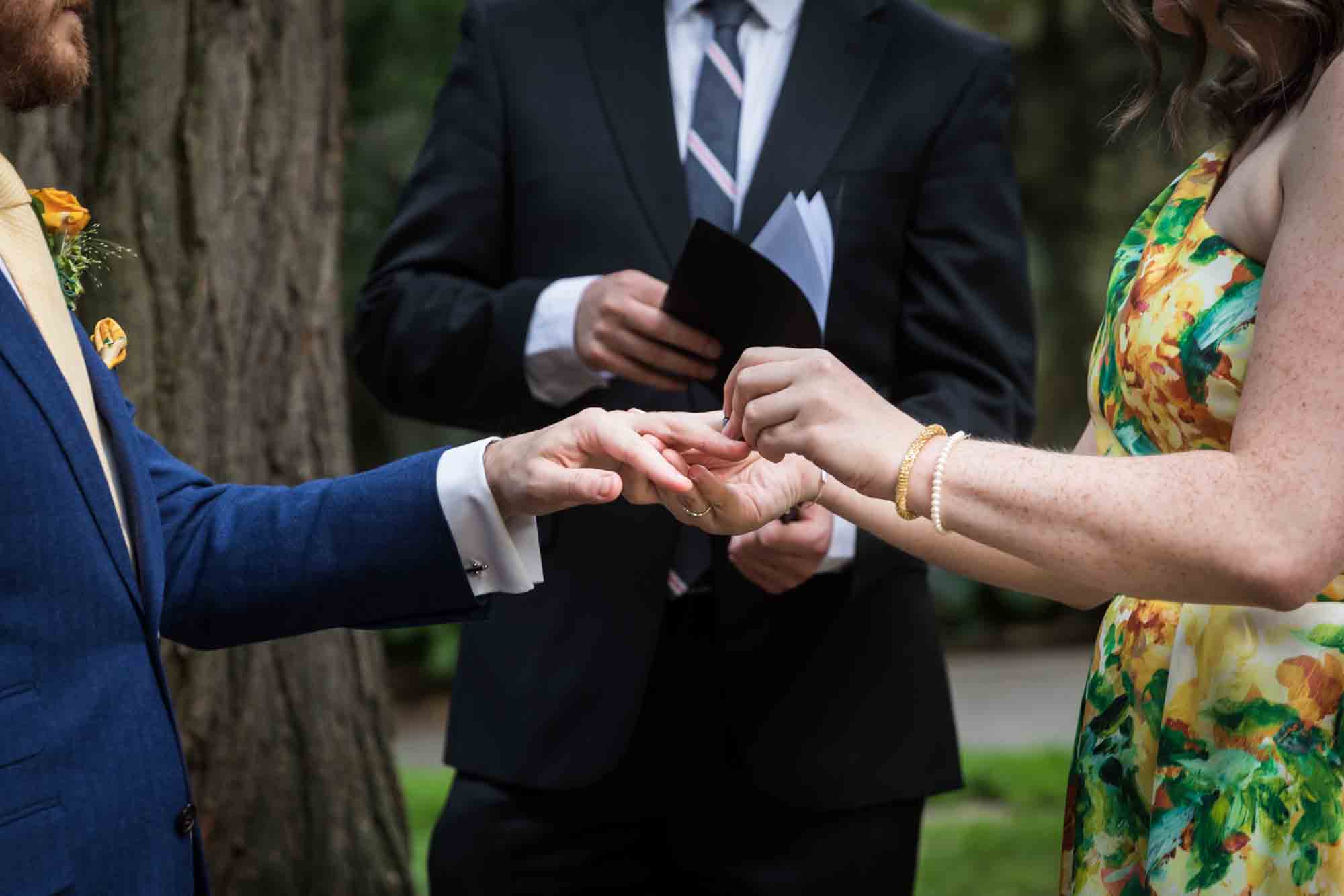 Close up of bride putting ring on groom's finger for an article on how to select a wedding date