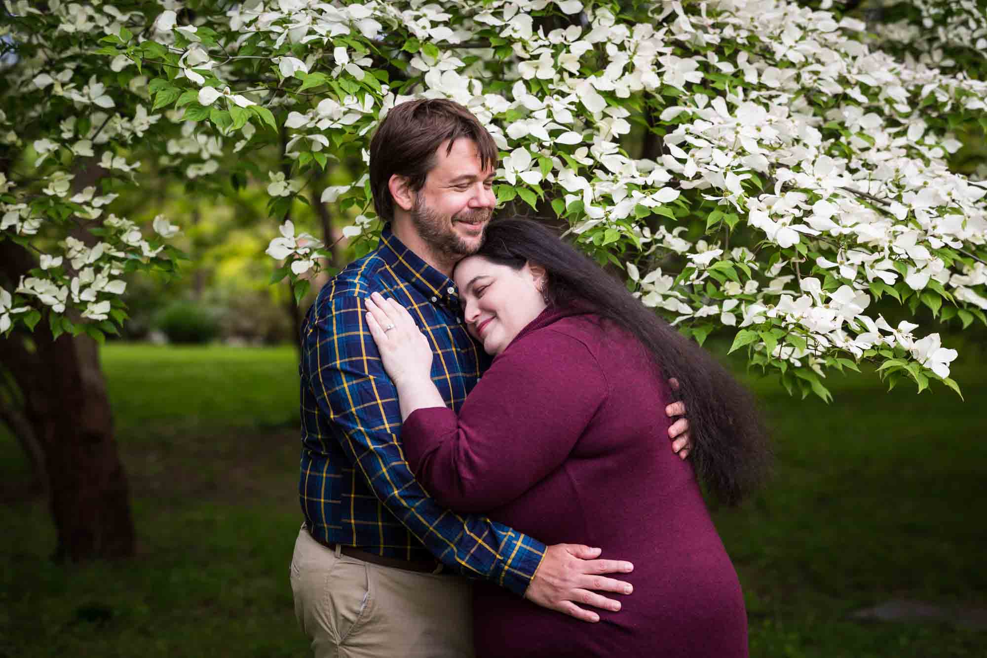Snug Harbor engagement photos of couple hugging in front of white dogwood tree