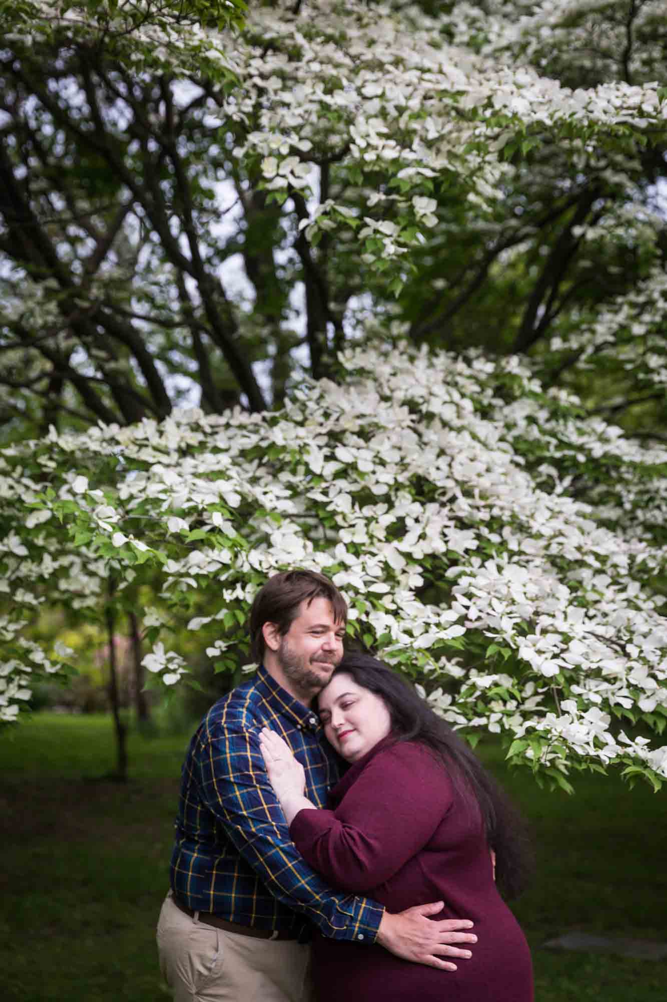 Snug Harbor engagement photos of couple hugging in front of white dogwood tree