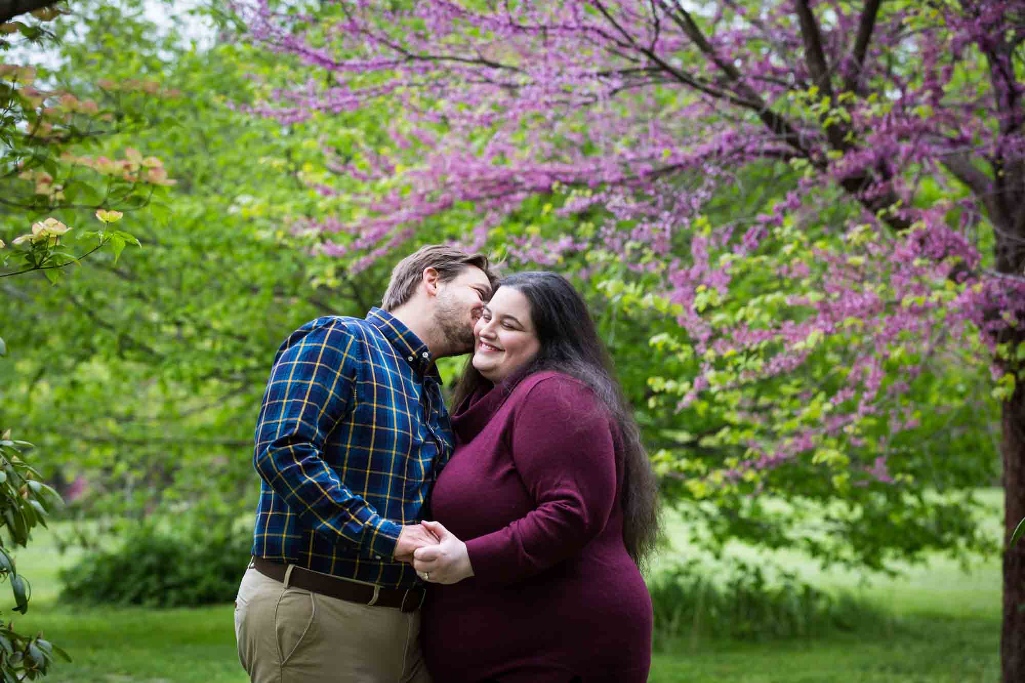 Snug Harbor engagement photos of man kissing woman's cheek in garden