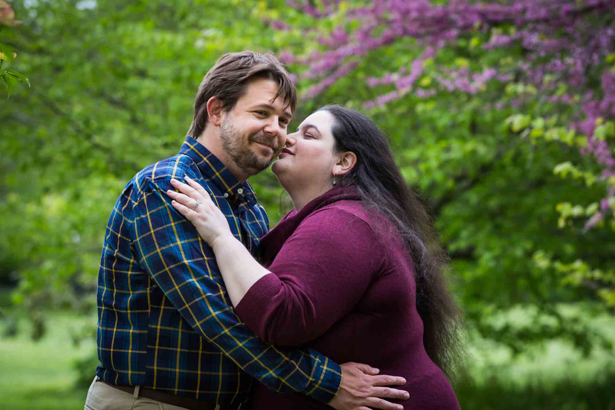 Snug Harbor engagement photos of woman kissing man's cheek in garden