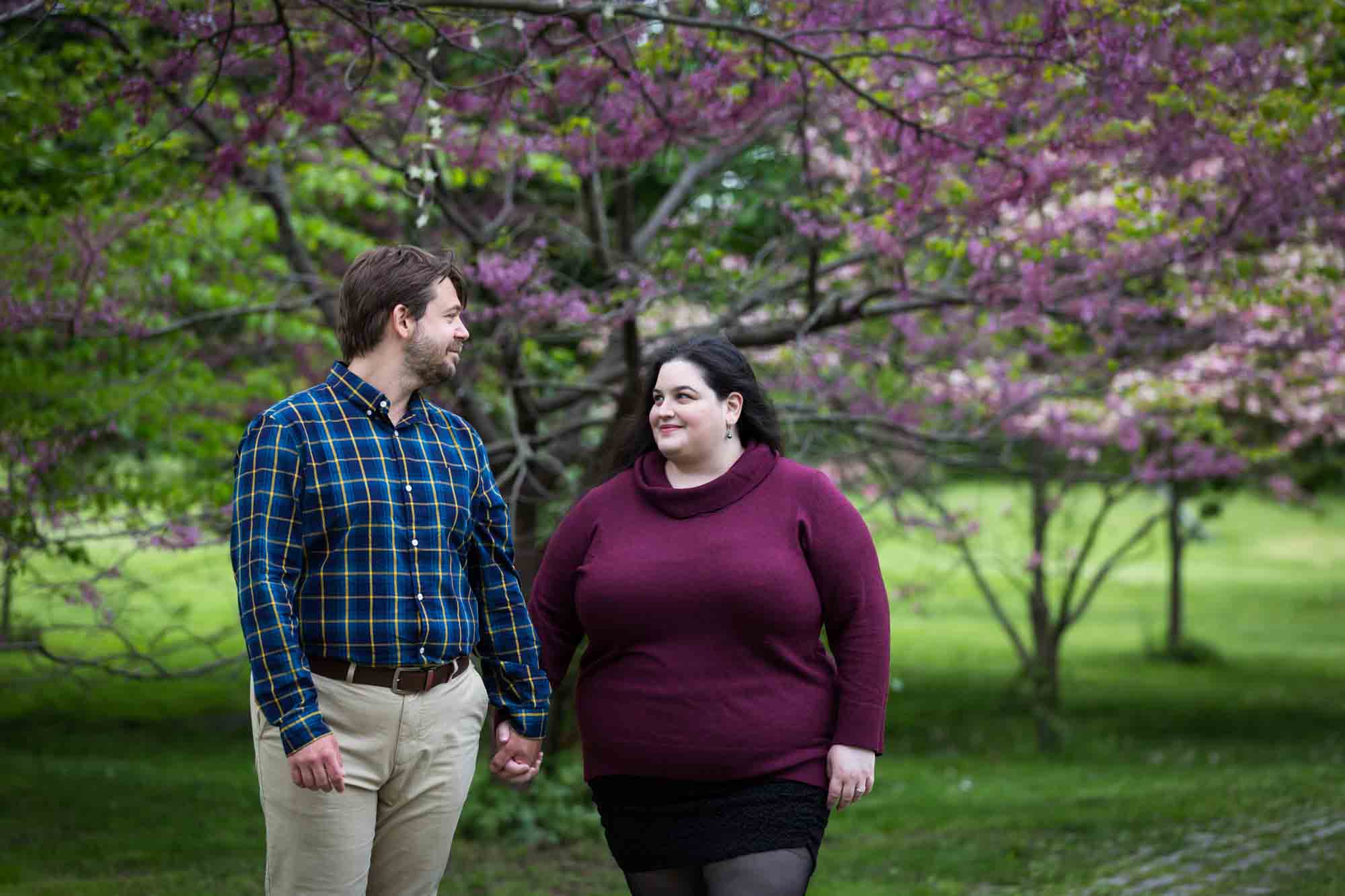 Snug Harbor engagement photos of couple holding hands in front of pink flowering tree