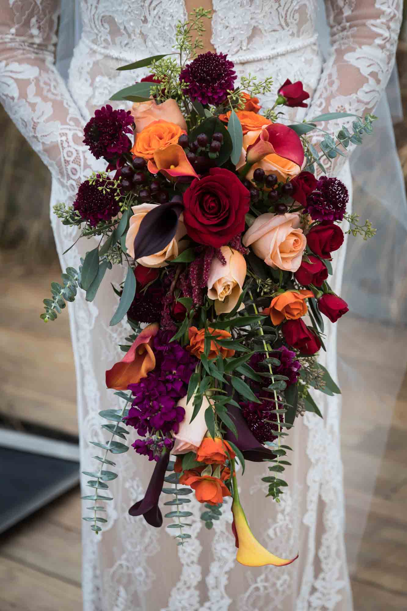 Close up on bride holding red and orange flower bouquet