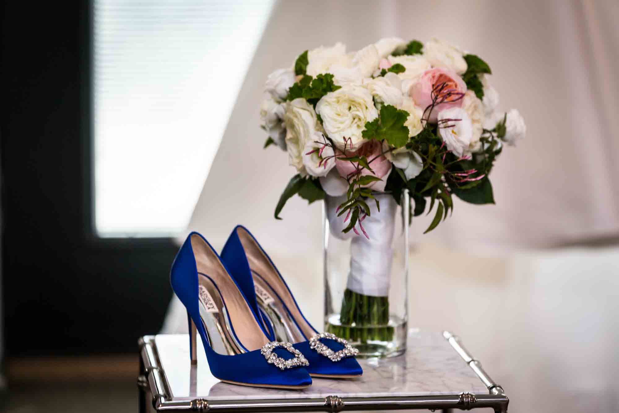 Table holding blue shoes with rhinestone clips and vase with pink flower bouquet