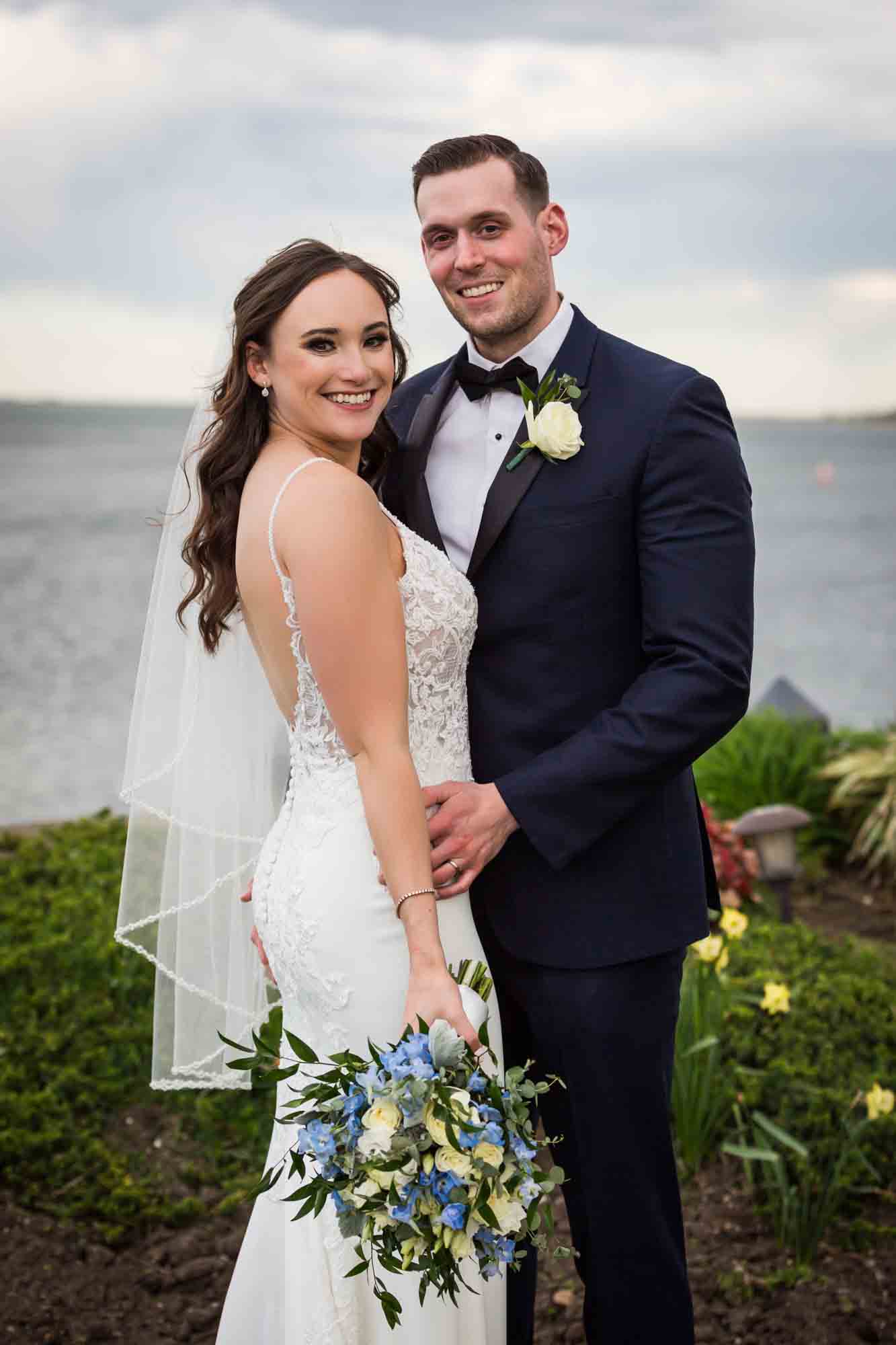 Bride waring sleeveless dress and groom holding bouquet in front of lake