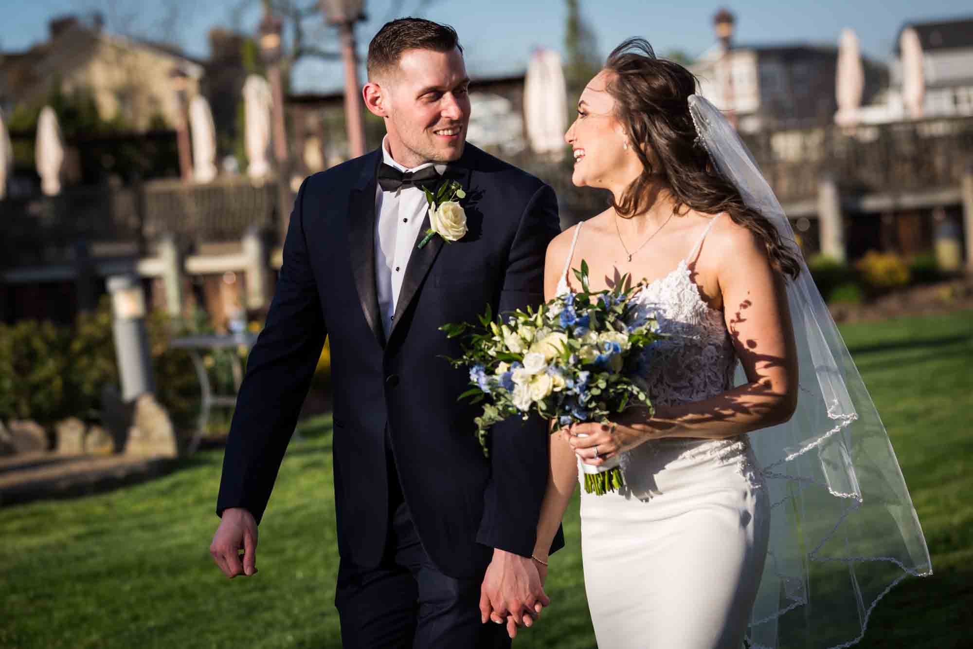 Bride holding bouquet and groom walking through garden