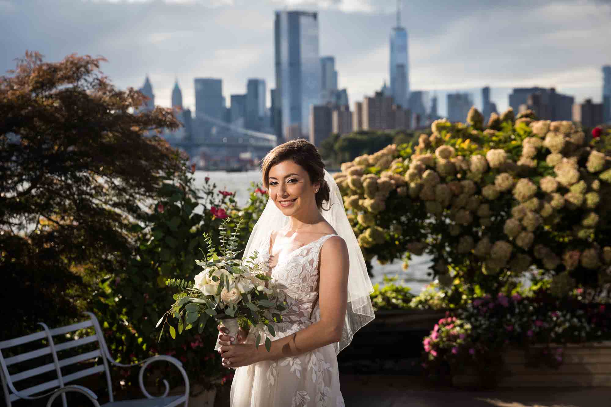 Bride holding bouquet in front of NYC skyline and waterfront