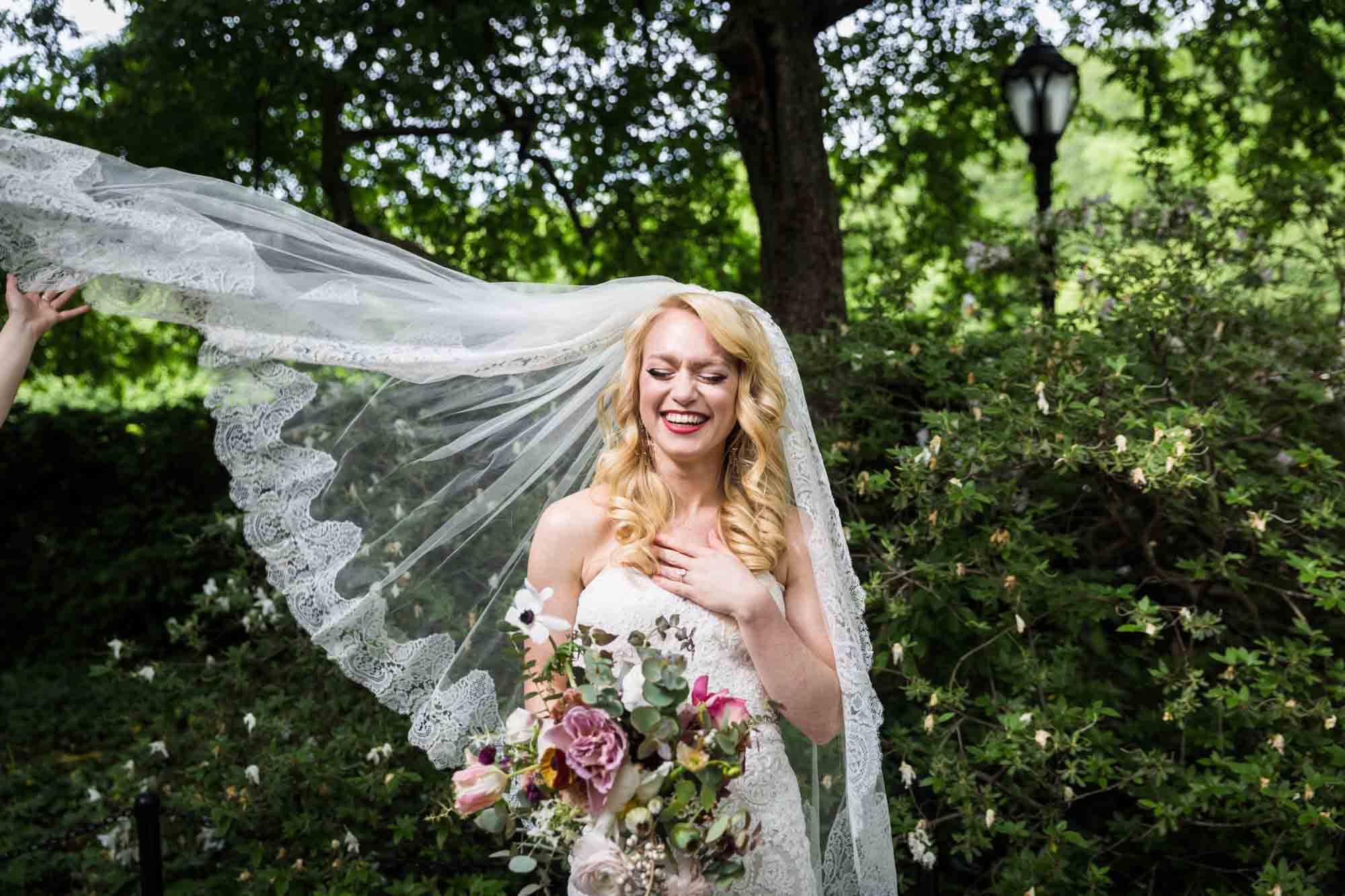 Bride holding bouquet and having veil fly off to the left in Central Park