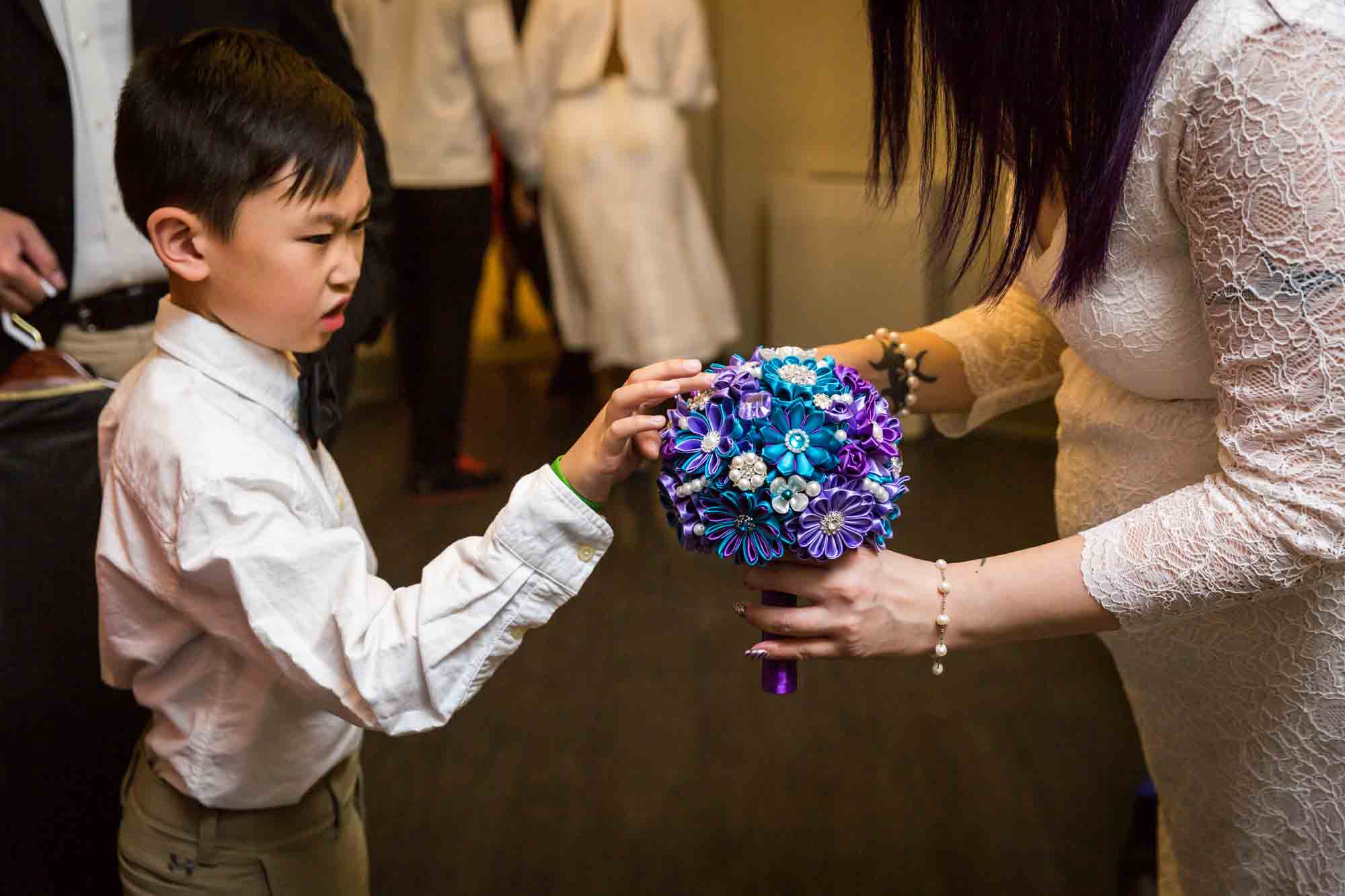 Bride holding bouquet of brooches out to young boy
