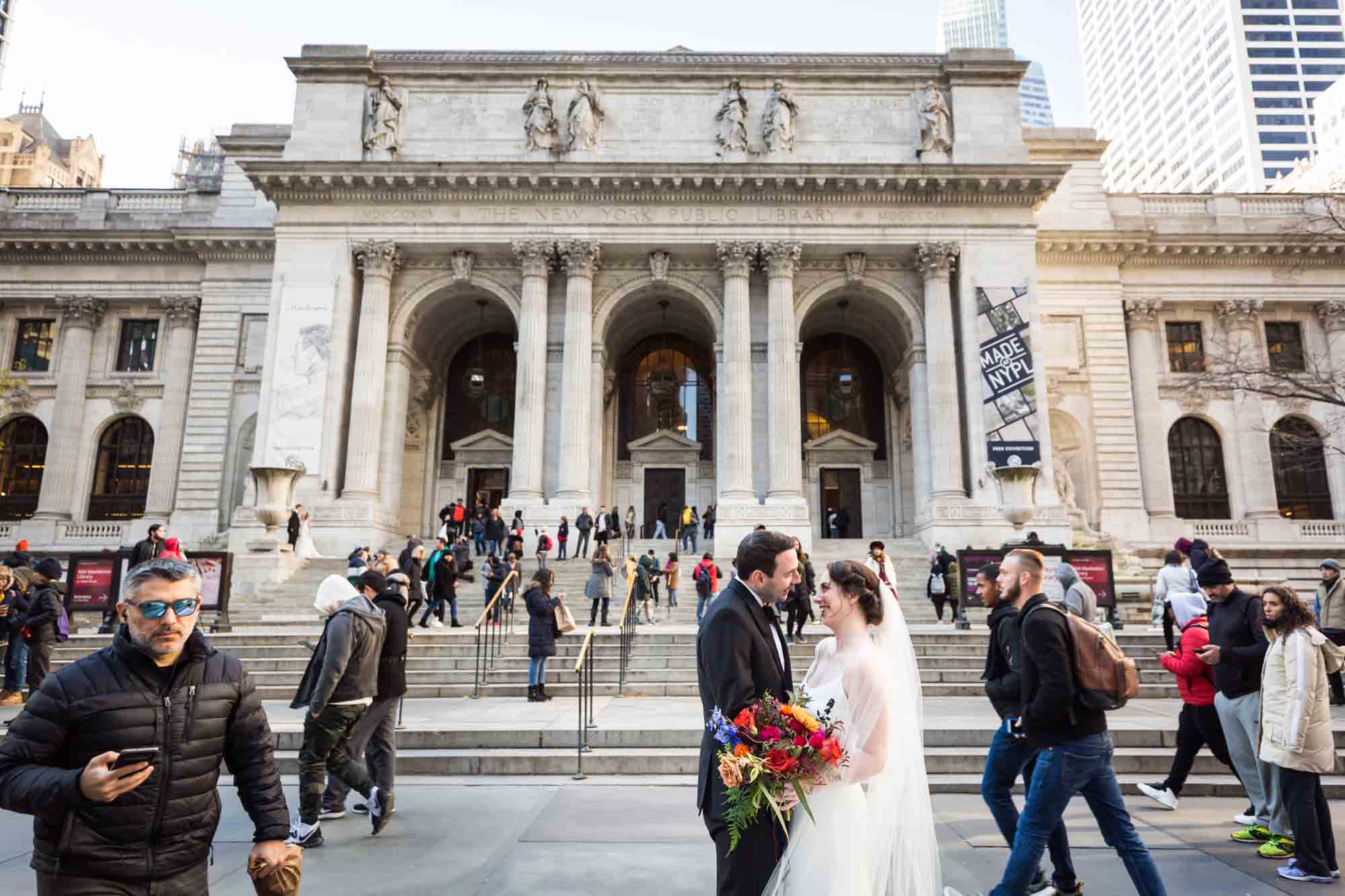 Bride and groom standing in front of NYC public library with crowd walking past