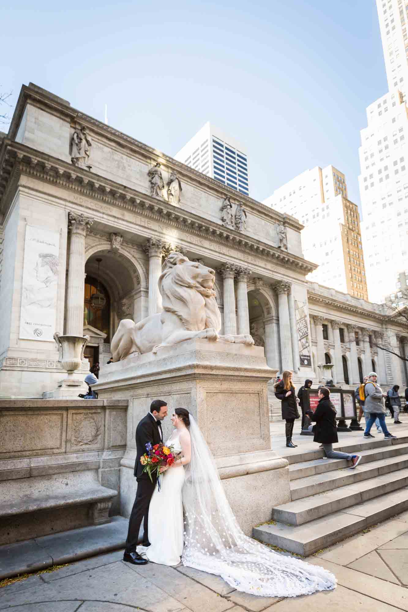 Bride and groom standing in front of lion statue in front of NYC public library