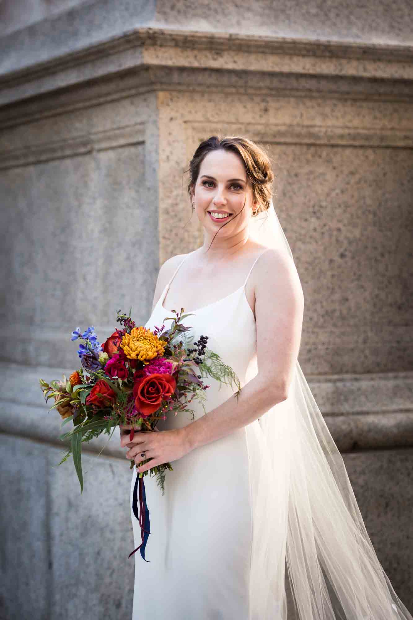 Bride holding colorful flower bouquet in front of stone building