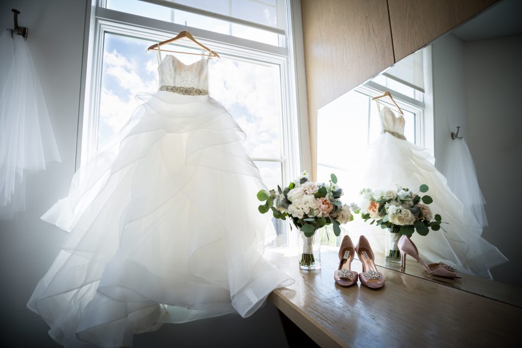 Wedding dress, bouquet, and shoes in front of window for article on wedding bouquet photo tips