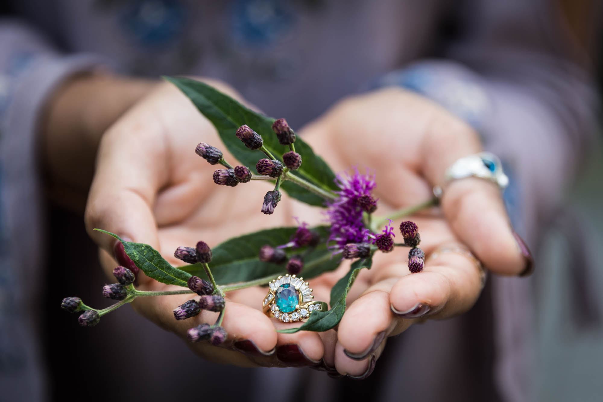 Woman's hands holding purple flower and engagement ring with green stone