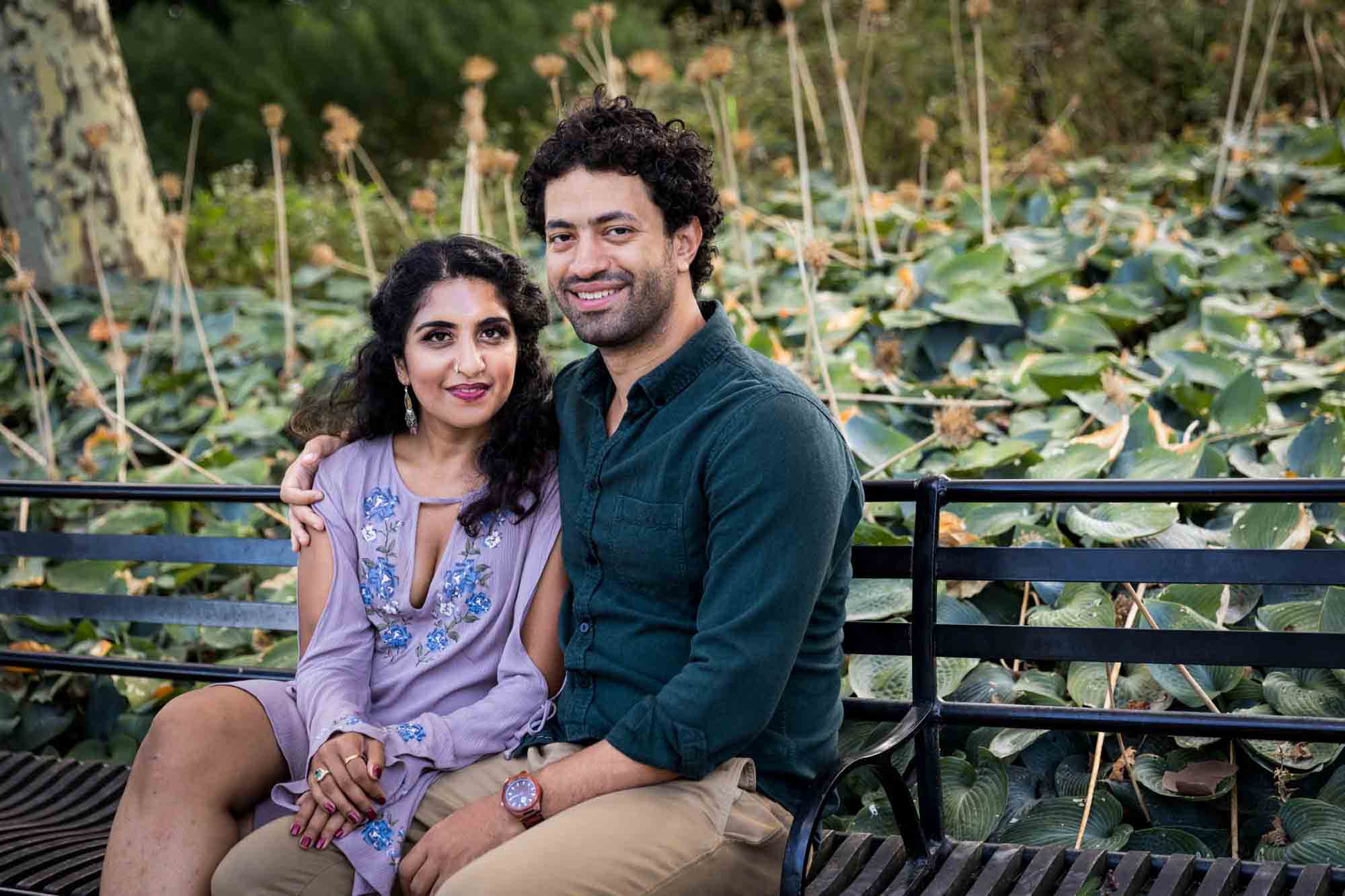 Battery Park engagement photos of couple sitting on bench in front of plants