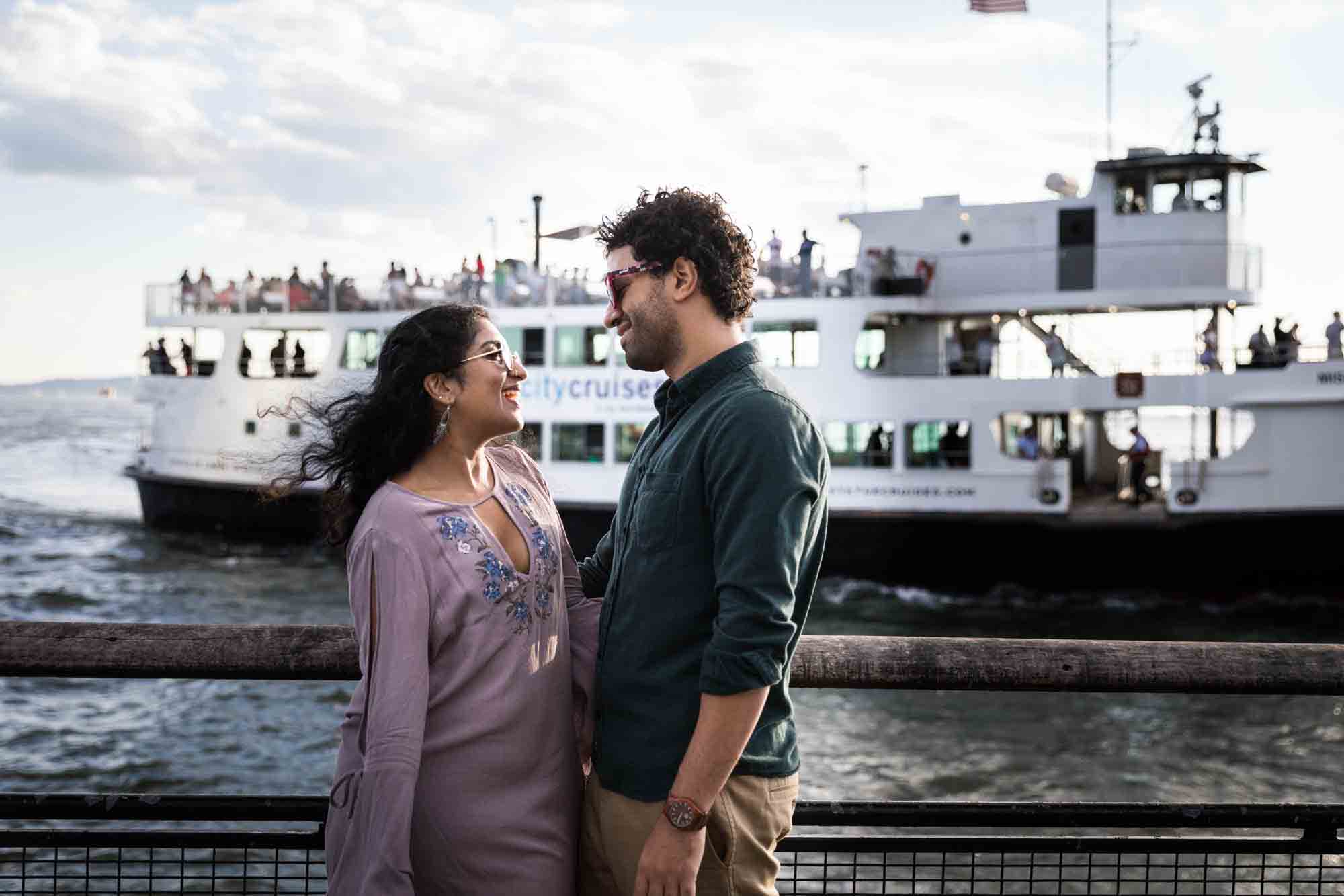 Battery Park engagement photos of couple standing along railing with ferry in background