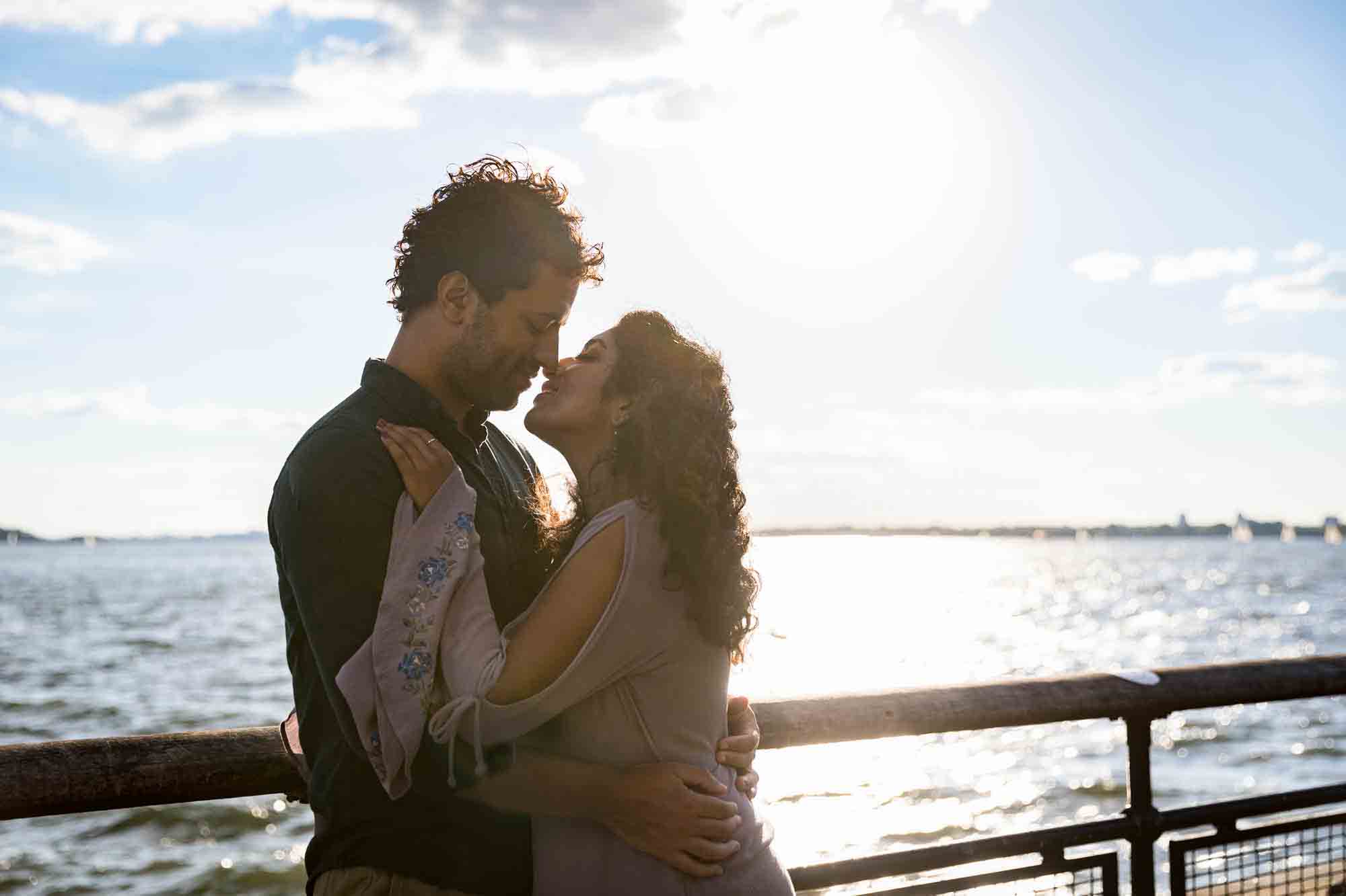 Battery Park engagement photos of couple hugging along railing with water in background