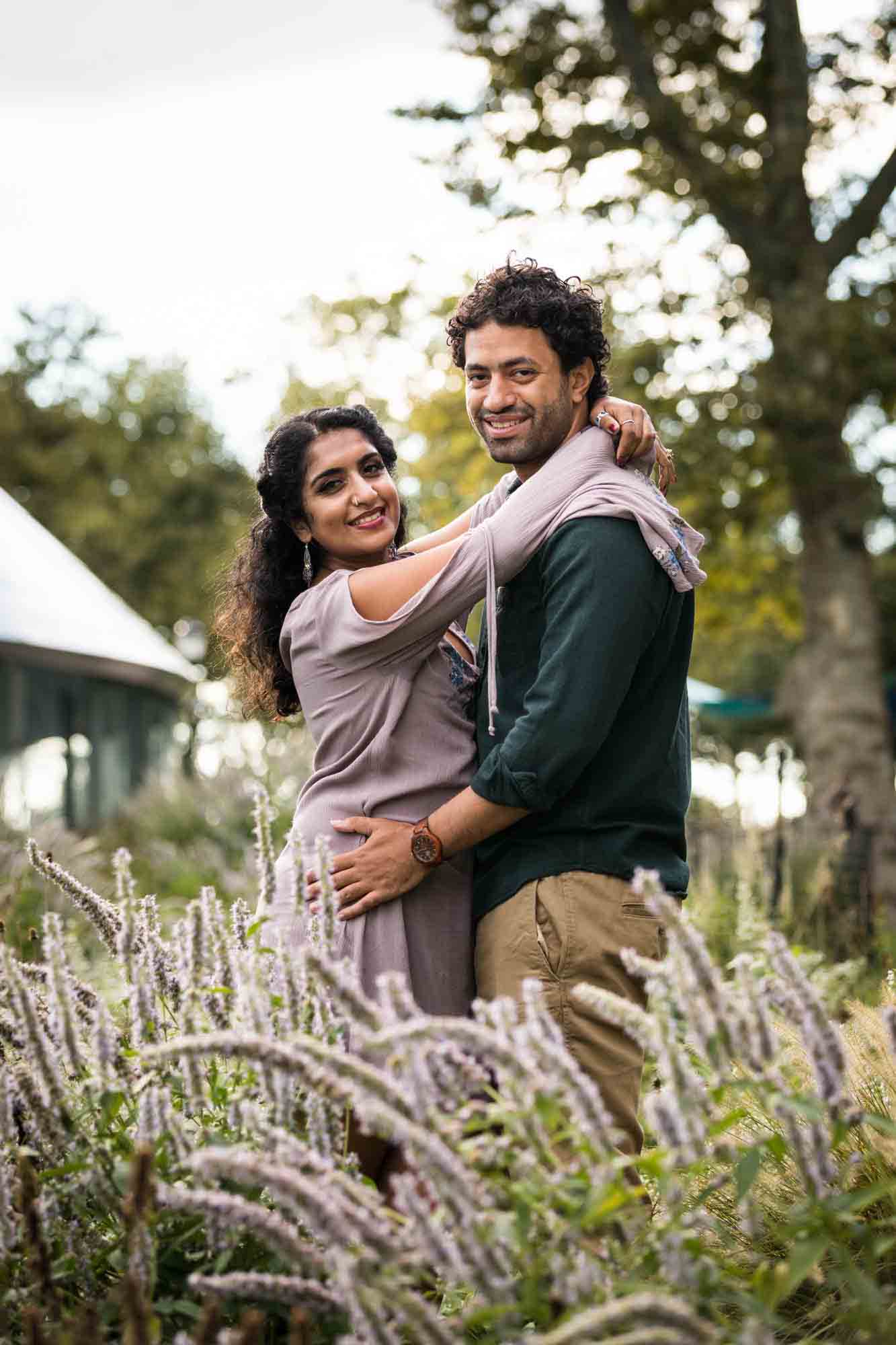 Battery Park engagement photos of couple hugging behind purple flowers