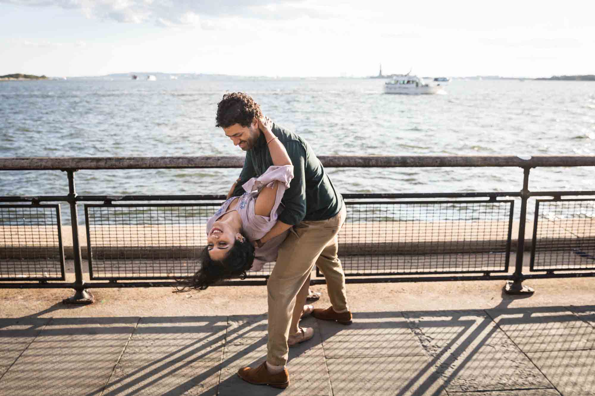 Battery Park engagement photos ofman dipping woman while dancing in front of NYC waterfront